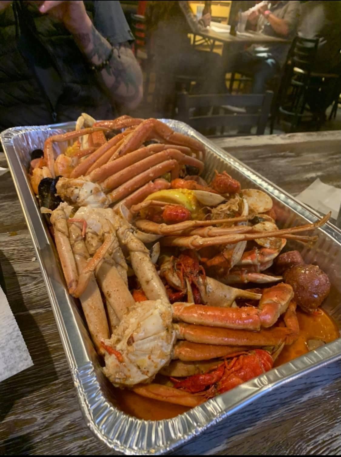 A large tray of assorted seafood including crabs, lobsters, shrimp, and crawfish, sitting on a wooden table at a restaurant.