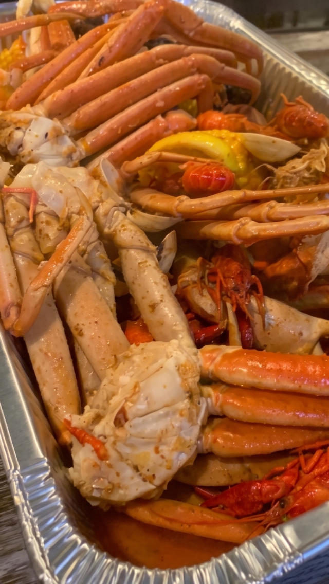 An aluminum tray filled with cooked seafood, including crabs, crawfish, and shrimp.