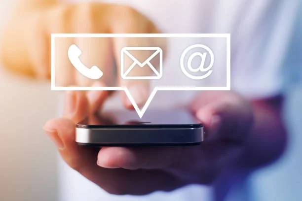 Person holder en smartphone med ikoner for telefon, email og webadresse over skærmen.