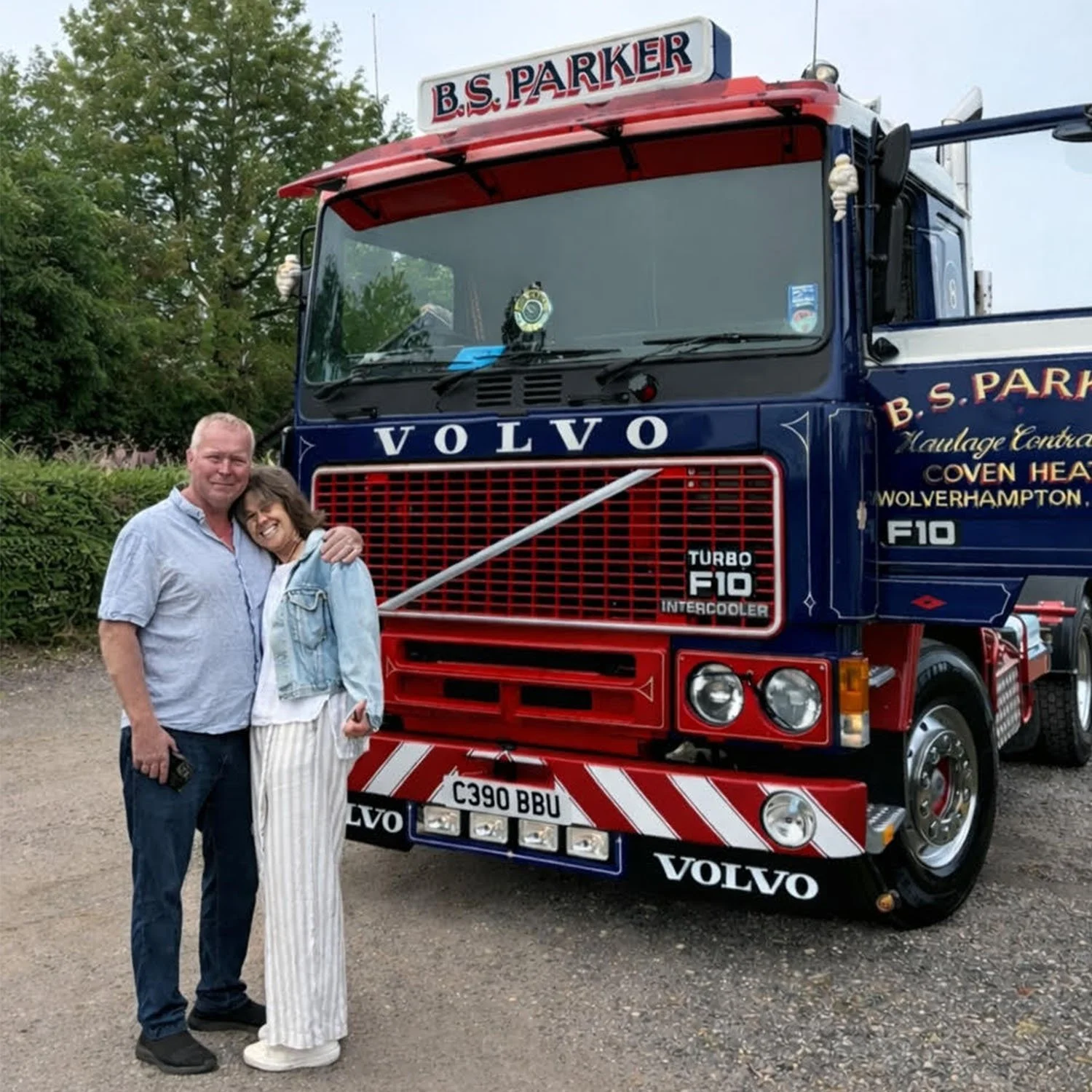 A smiling man and woman embracing each other in front of a large vintage Volvo fire truck with