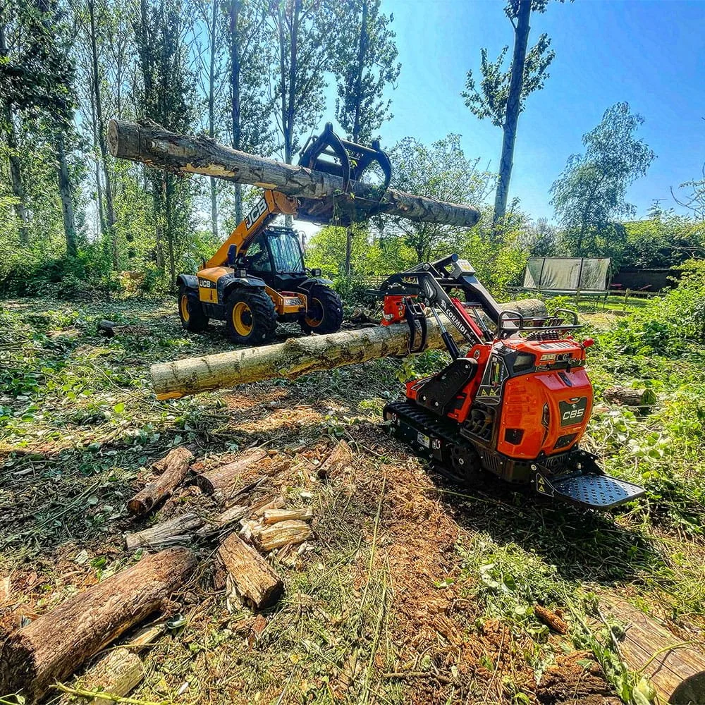 A toy JCB small construction machine lifting a large fallen tree log in a wooded area.