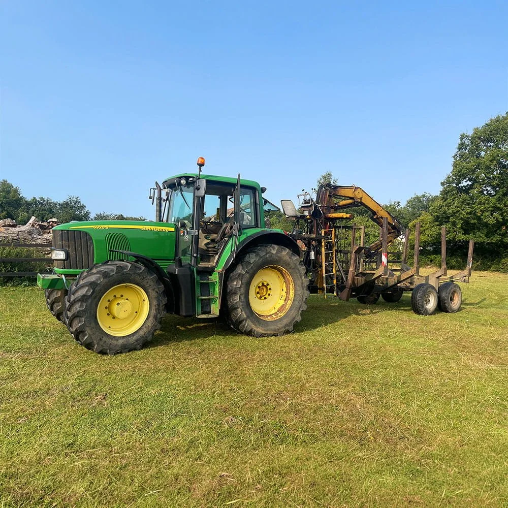 A green tractor with yellow wheels is parked on a grassy field, attaching a large agricultural implement with wheels.