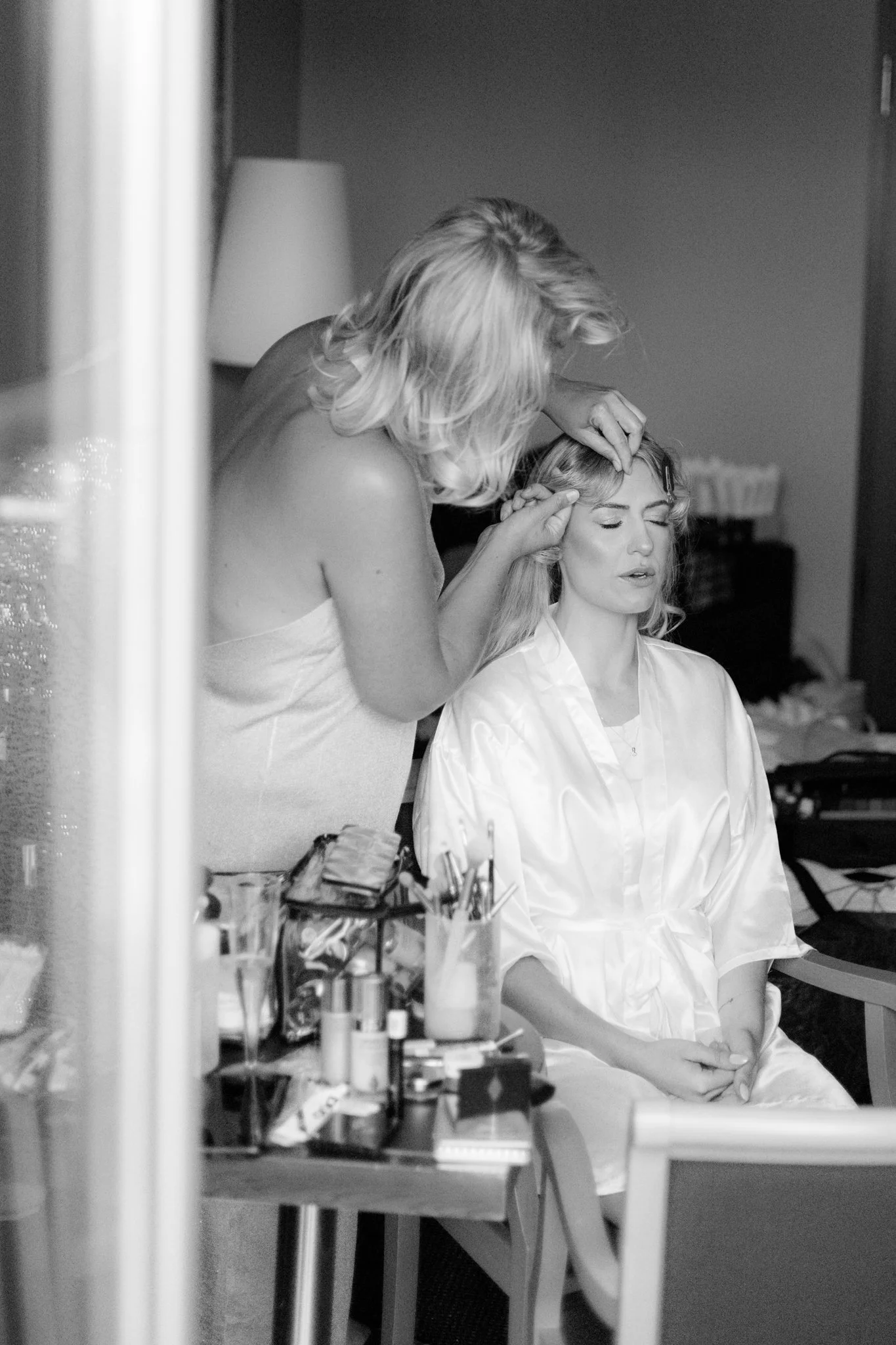 Frau erhält im Wohnzimmer eine Make-up-Anleitung von einer Stylistin, die Make-up-Produkte auf einem Tisch neben ihnen stehen.