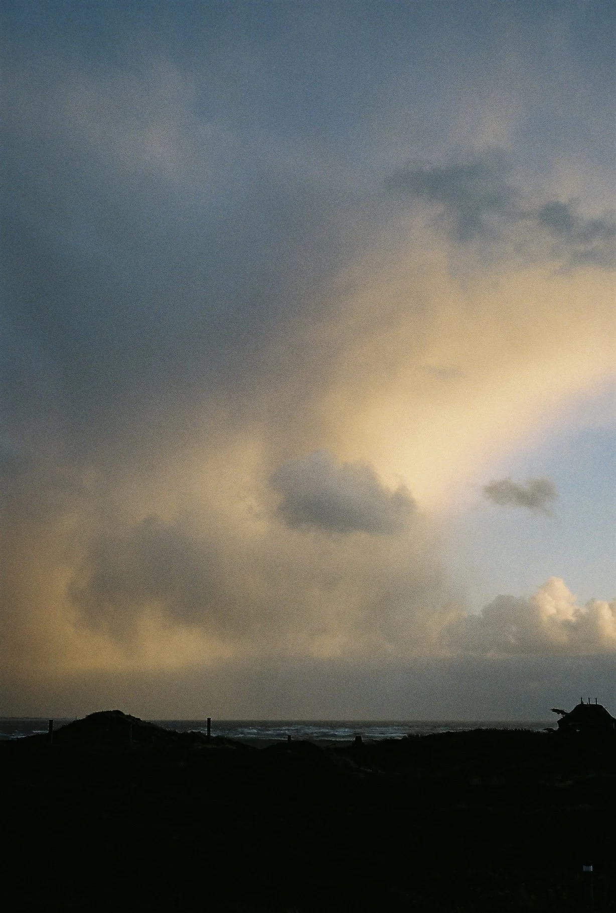 Ein düsterer Himmel über dem Meer mit dunklen Wolken und einer lightly beleuchteten Küstenlinie im Vordergrund.