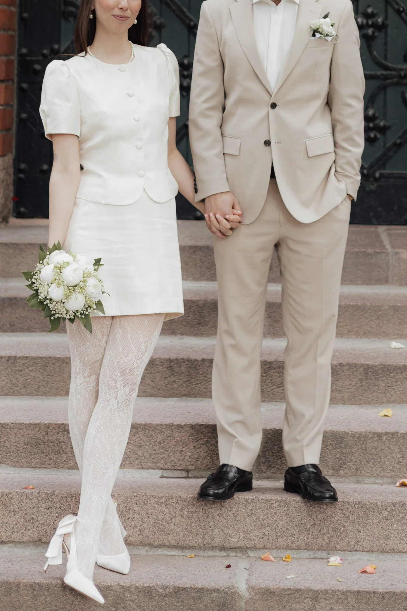 Das Brautpaar nach ihrer Standesamtlichen Hochzeit in Berlin steht auf einer Treppe vor dem Standesamt und hält sich an den Händen.