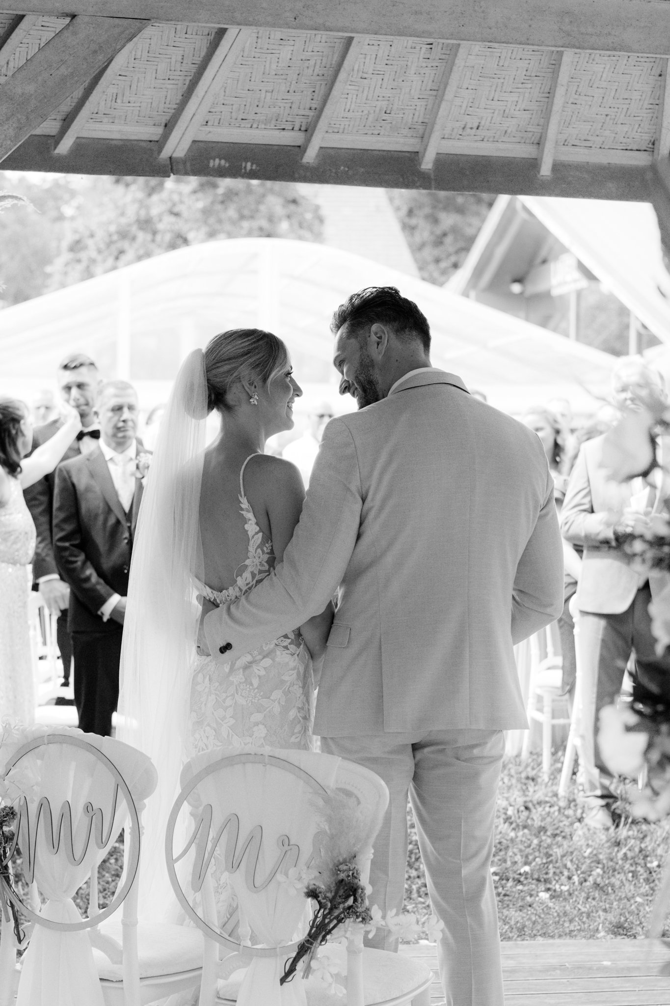 Braut und Bräutigam beim Hochzeitstanz im Freien, im Hintergrund stehen Hochzeitsgäste, oben Dachbalken mit gewebtem Sattela.