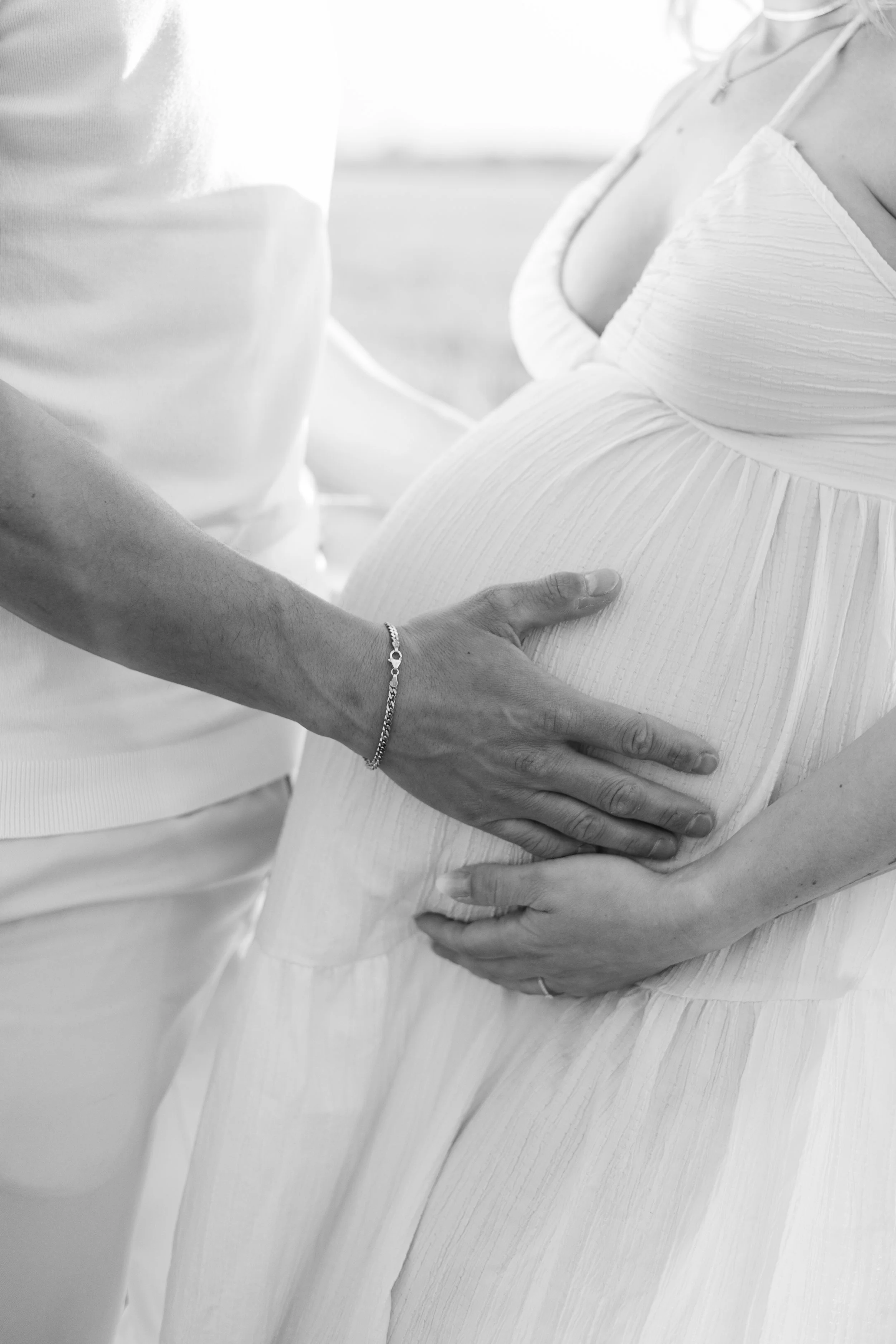 Schwangere Frau in einem weißen Kleid, die von einer anderen Person gestützt wird.