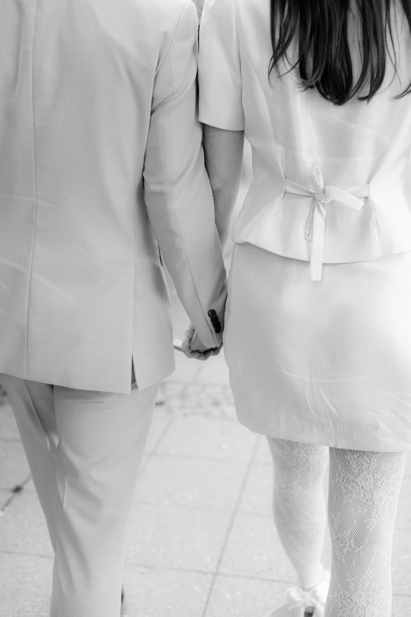 Ein Brautpaar hält Händchen, die Frau trägt ein weißes Hochzeitskleid und der Mann trägt einen hellen Anzug.