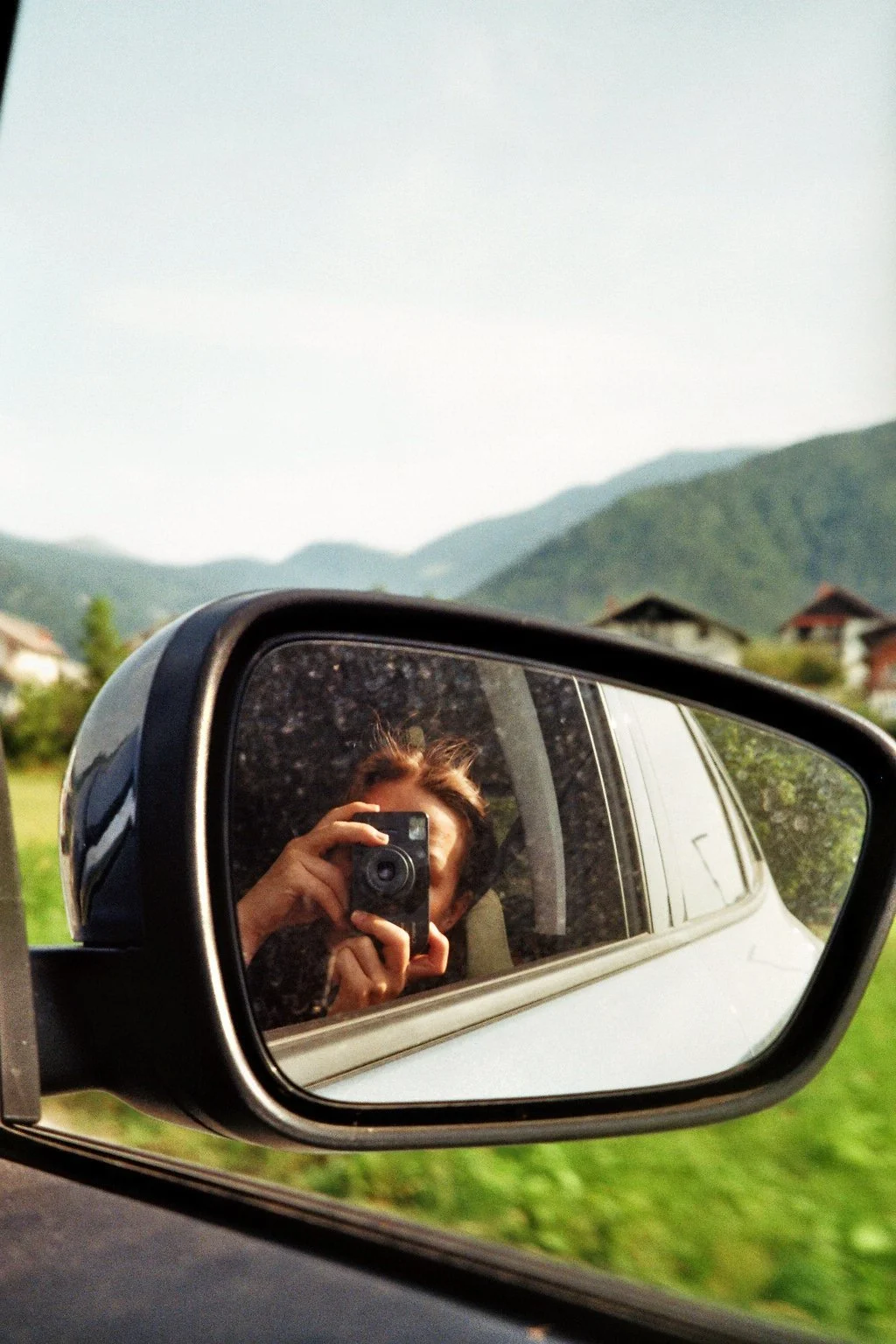 Der Blick in den Rückspiegel eines Autos, in dem eine Person ein Foto macht, mit Bergen im Hintergrund.