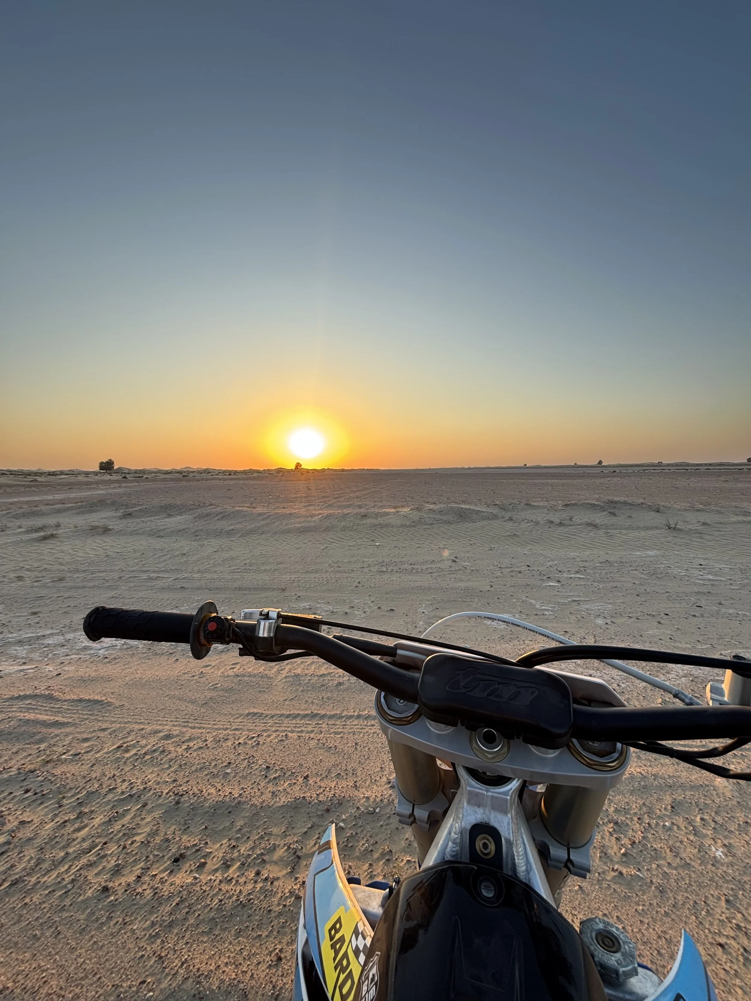 Motorcycle handlebar with a view of a desert landscape at sunset in the background.