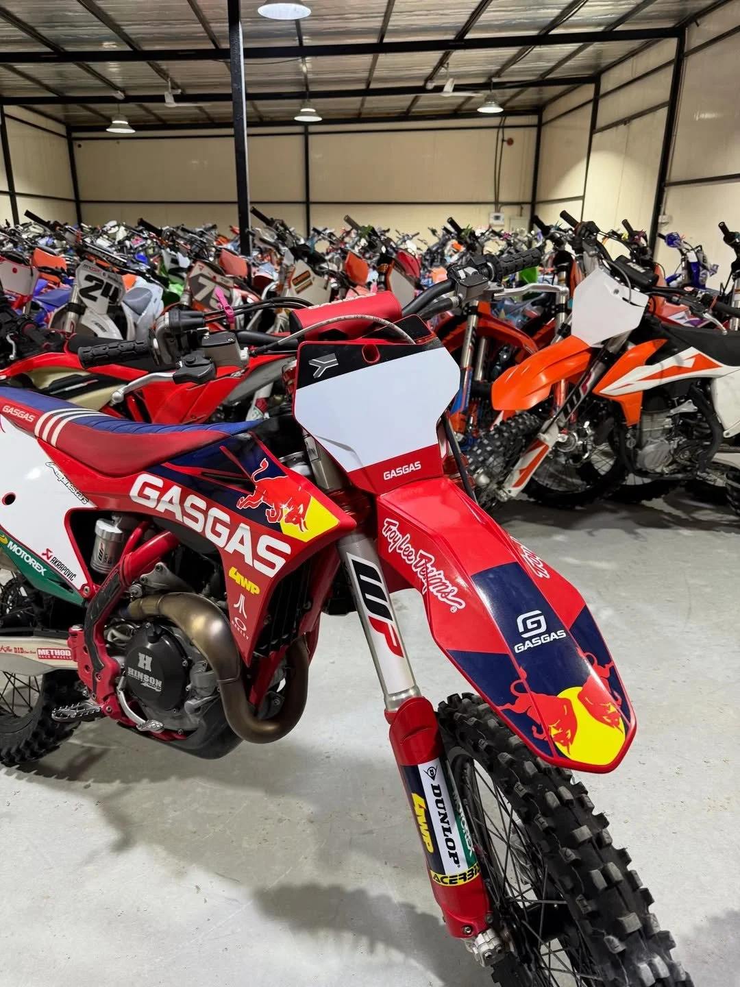 A collection of motocross dirt bikes in a storage facility, with a red and blue GasGas bike in the foreground.