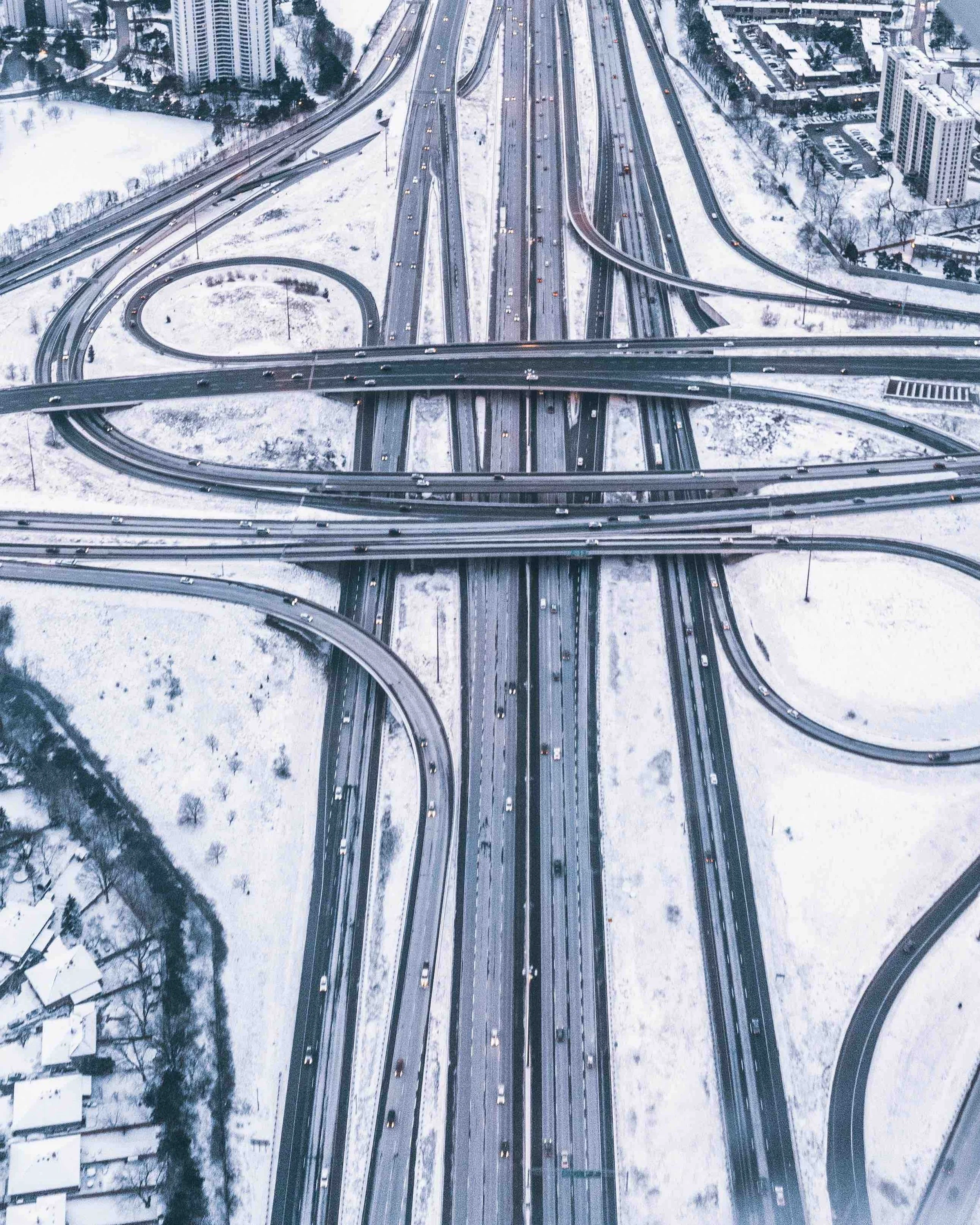 Aerial view of a complex multi-level highway interchange in winter, with looping ramps and snow-covered ground surrounding the roads.