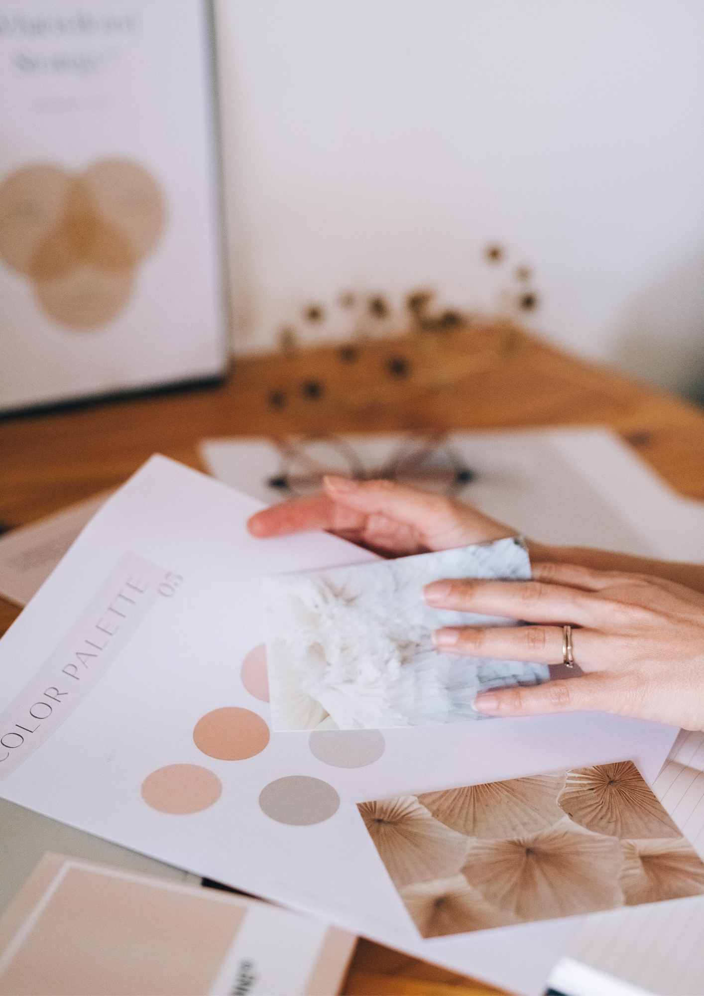 Close-up of a hand holding a booklet titled 'Color Palette for Palettes,' with a background of various sample color palettes and magazine pages on a table.