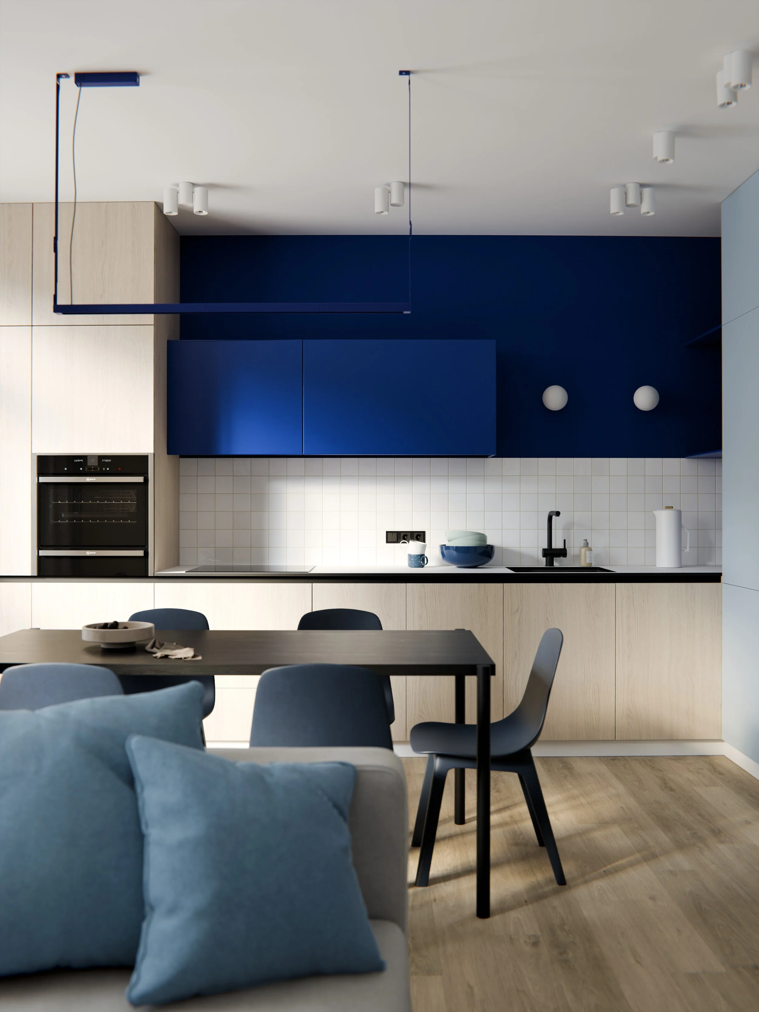 Interno di una cucina moderna con pareti bianche e blu, armadi in legno chiaro, piano di lavoro nero, e tavolo con sedie blu, alcune ciotole sul piano e tende nere alle finestre.