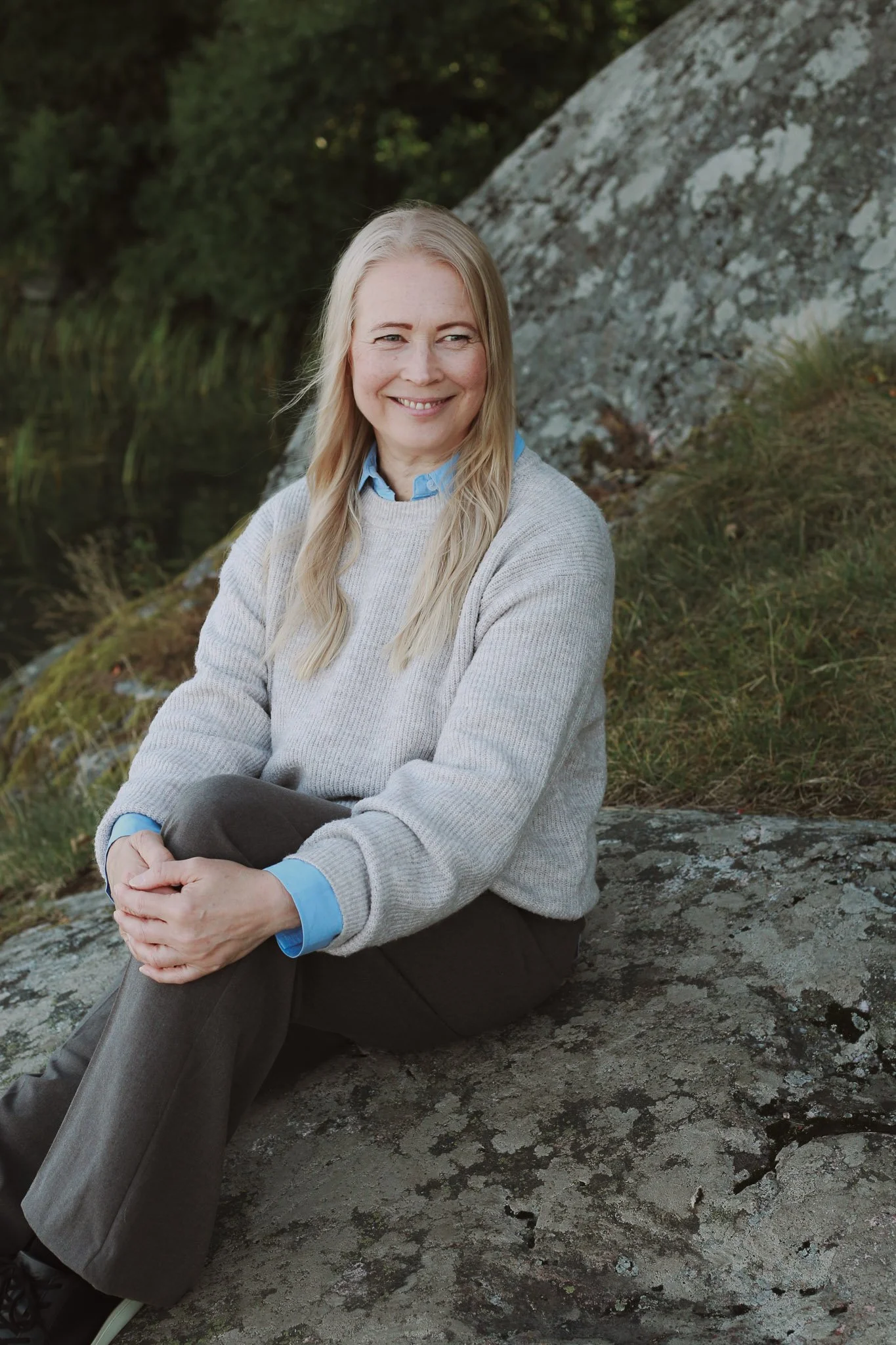 Mira Mustonen istuu kalliolla ja katsoo kohti hymyillen.
