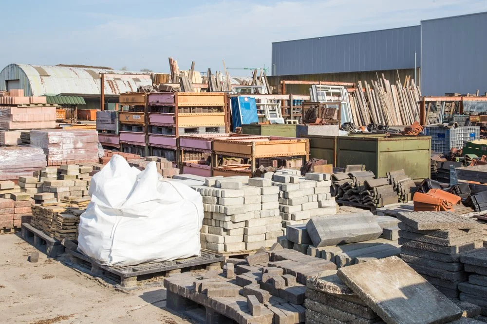 Outdoor construction materials including bricks, pavers, pallets, and metal storage containers at a building site or hardware yard.