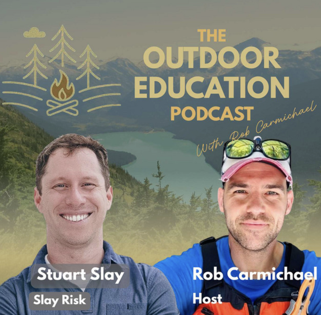 Podcast cover image featuring two men outdoors with mountains in the background. The left man has short brown hair, wearing a blue shirt, labeled 'Stuart Slay, Slay Risk.' The right man has a cap with sunglasses on top, wearing a blue shirt and orange vest, labeled 'Rob Carmichael, Host.' The title reads 'The Outdoor Education Podcast' with a mountain and forest illustration.