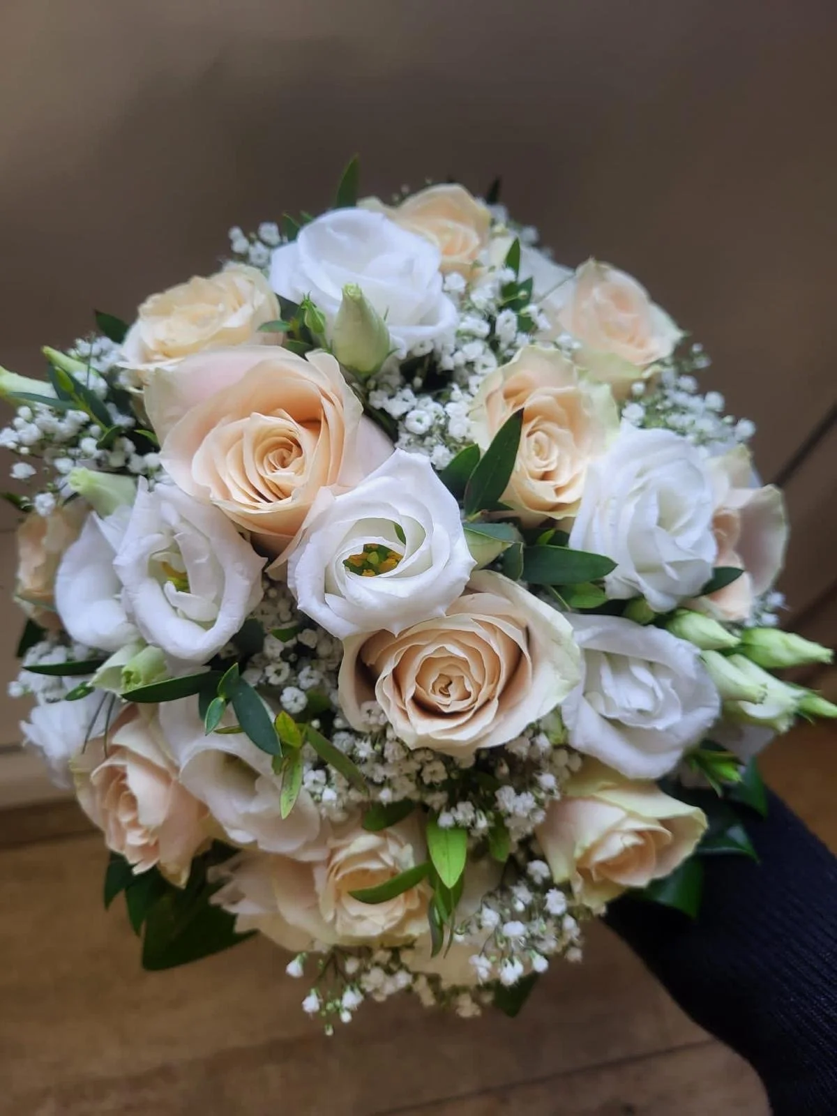 Ein Blumenstrauß mit cremefarbenen Rosen, weißen Blumen und grünen Blättern.