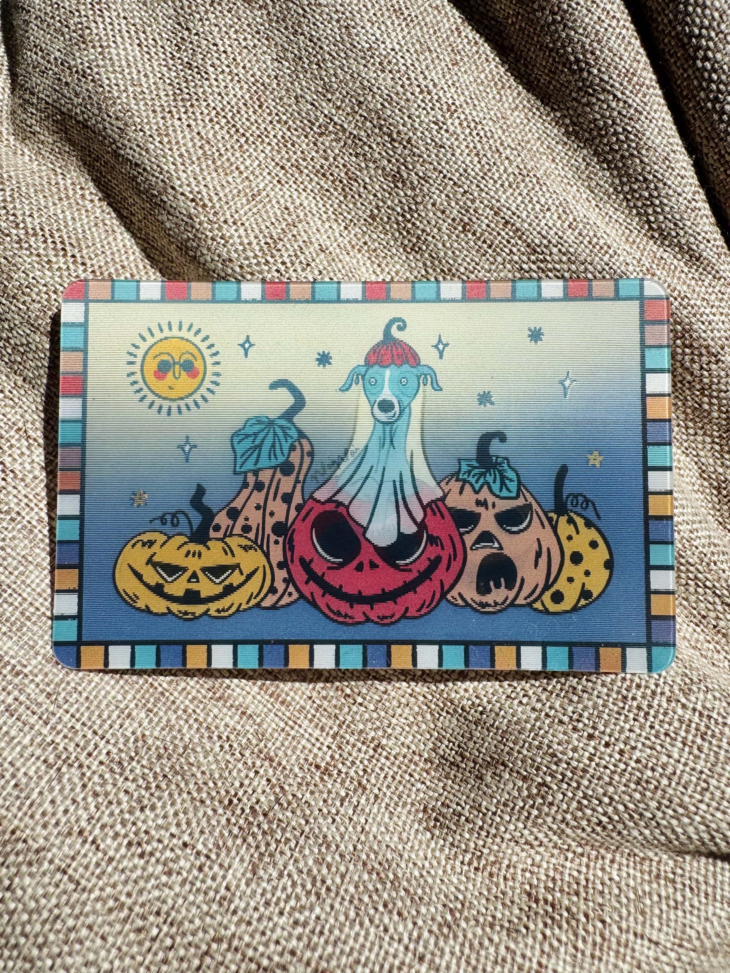 Colorful Halloween-themed lenticular card featuring a smiling Italian Greyhound blue dog wearing a pumpkin hat, surrounded by pumpkins, a smiling sun, and stars, on a checkered border background.