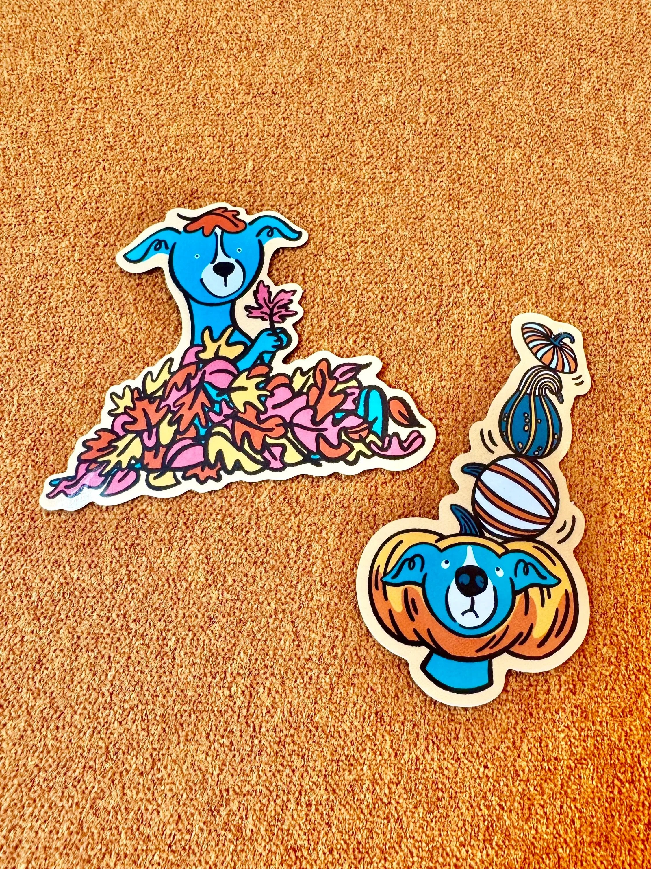 Colorful cartoon animal stickers on orange background, including a blue dog covered in leaves and a blue dog balancing pumpkins on its head.