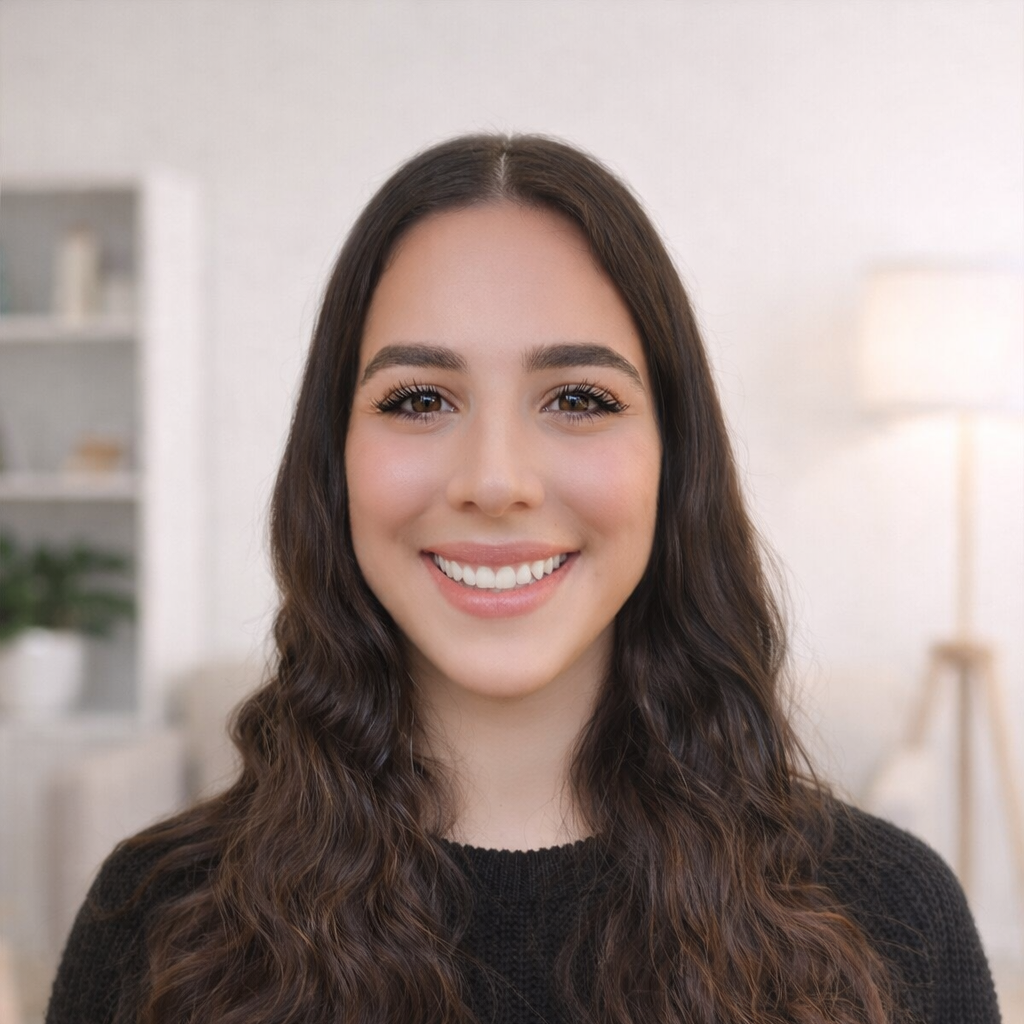 A young woman with long, dark, wavy hair smiling in a well-lit room. a senior mental health medical secretary in our adhd, autism and general psychiatry team.