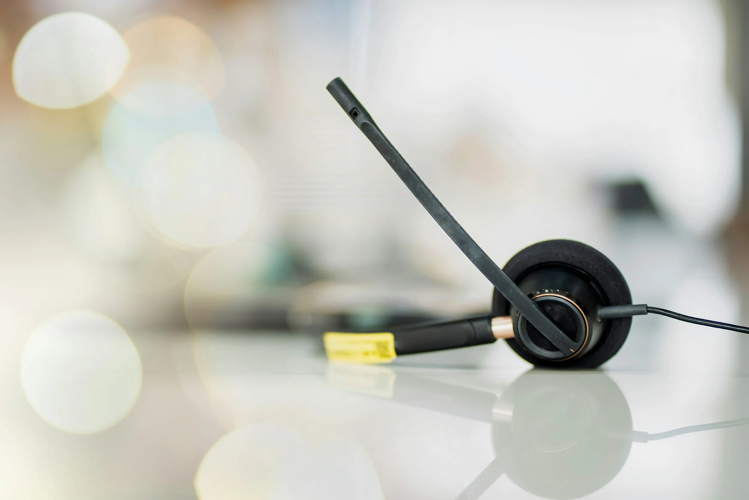 Close-up of a black microphone with a foam cover, mounted on a microphone stand with a yellow tag, against a blurred background.