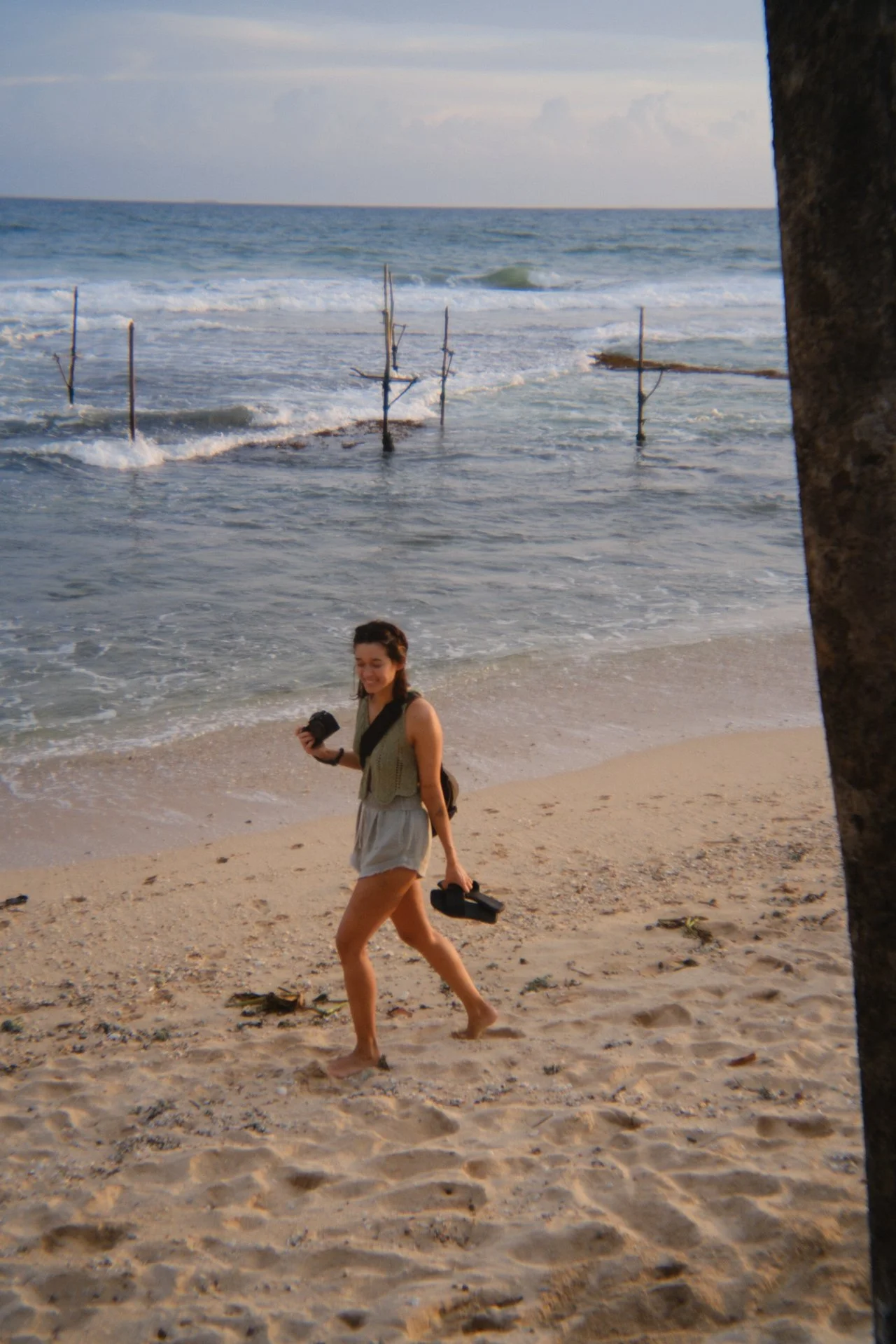 Kate Bryant walking along a beach with camera equipment while documenting coastal culture and travel stories.