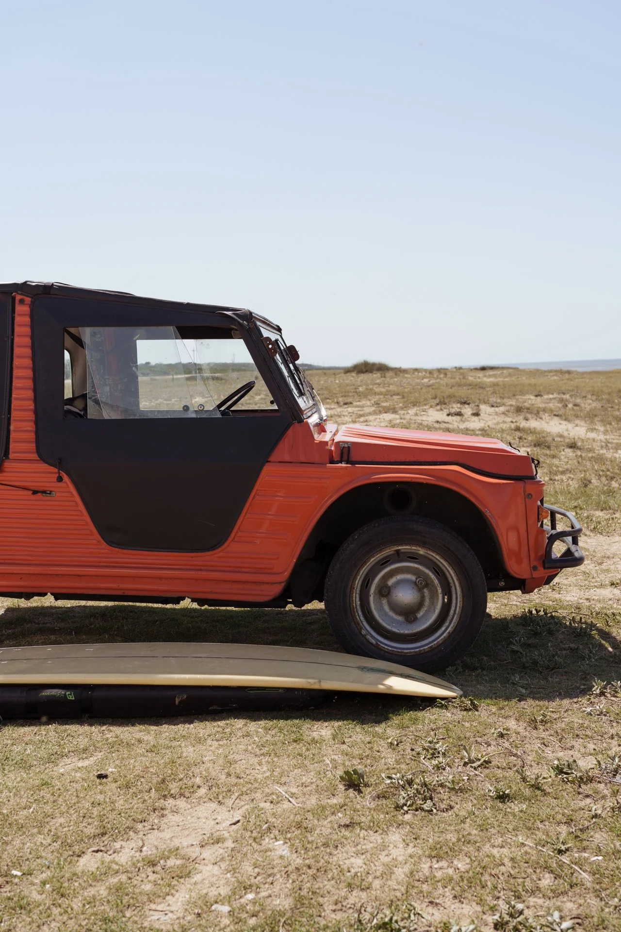 Vintage orange vehicle parked beside a coastal beach under clear skies.