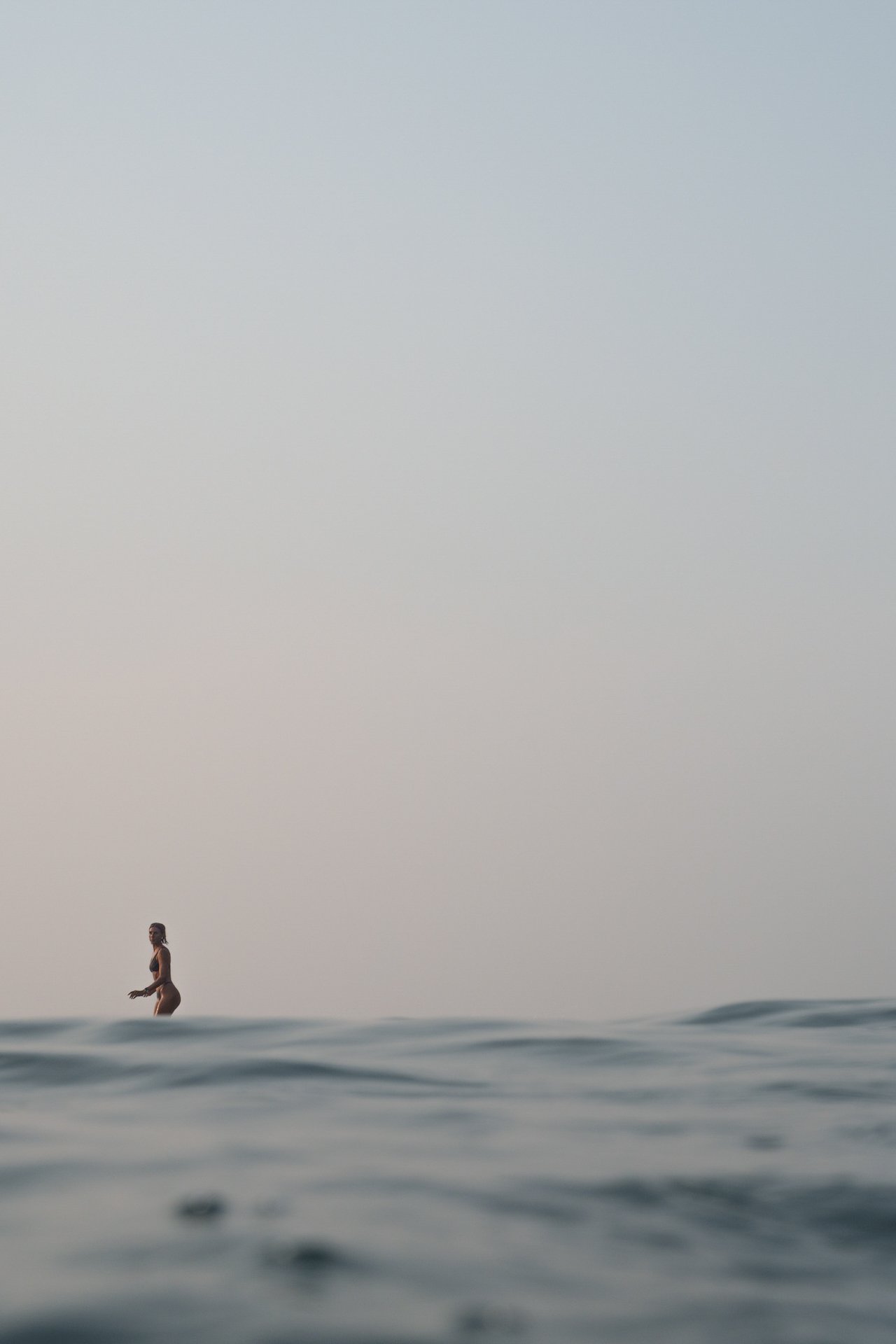 Woman surfing in the ocean beneath an open coastal sky.