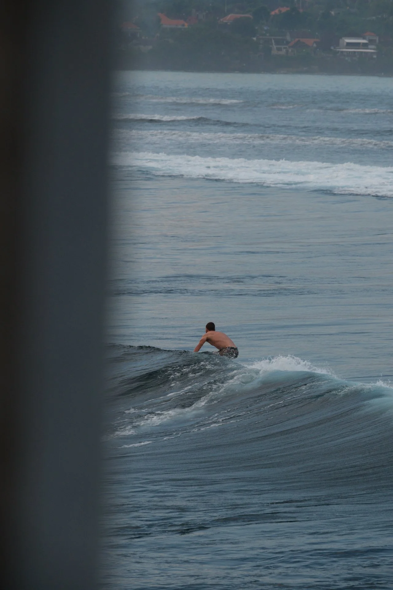 Surfer riding a wave framed by a coastal window overlooking the ocean.