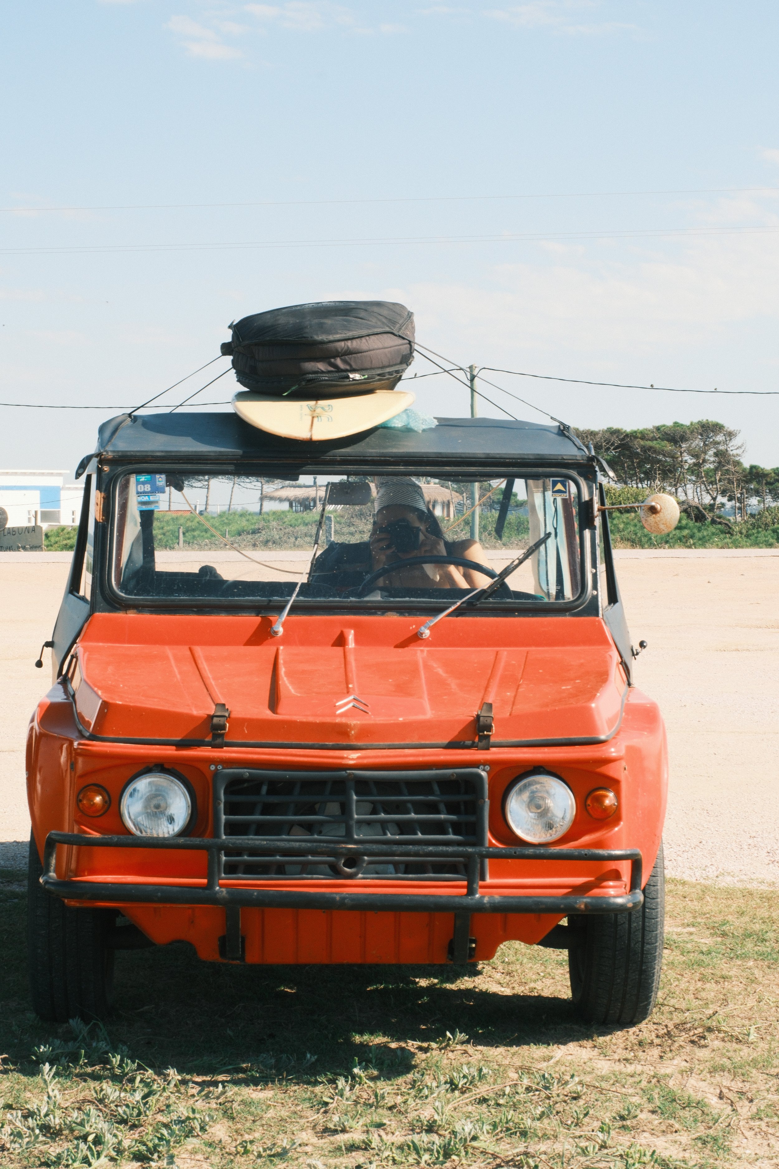 Self-portrait of photographer Kate Bryant sitting inside a vintage orange Citroën Mehari with surfboards strapped to the roof, photographed in Uruguay.