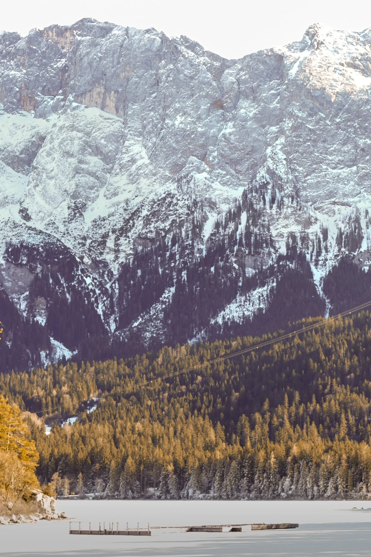 Snow-capped mountain range above a frozen lake with forested shoreline.
