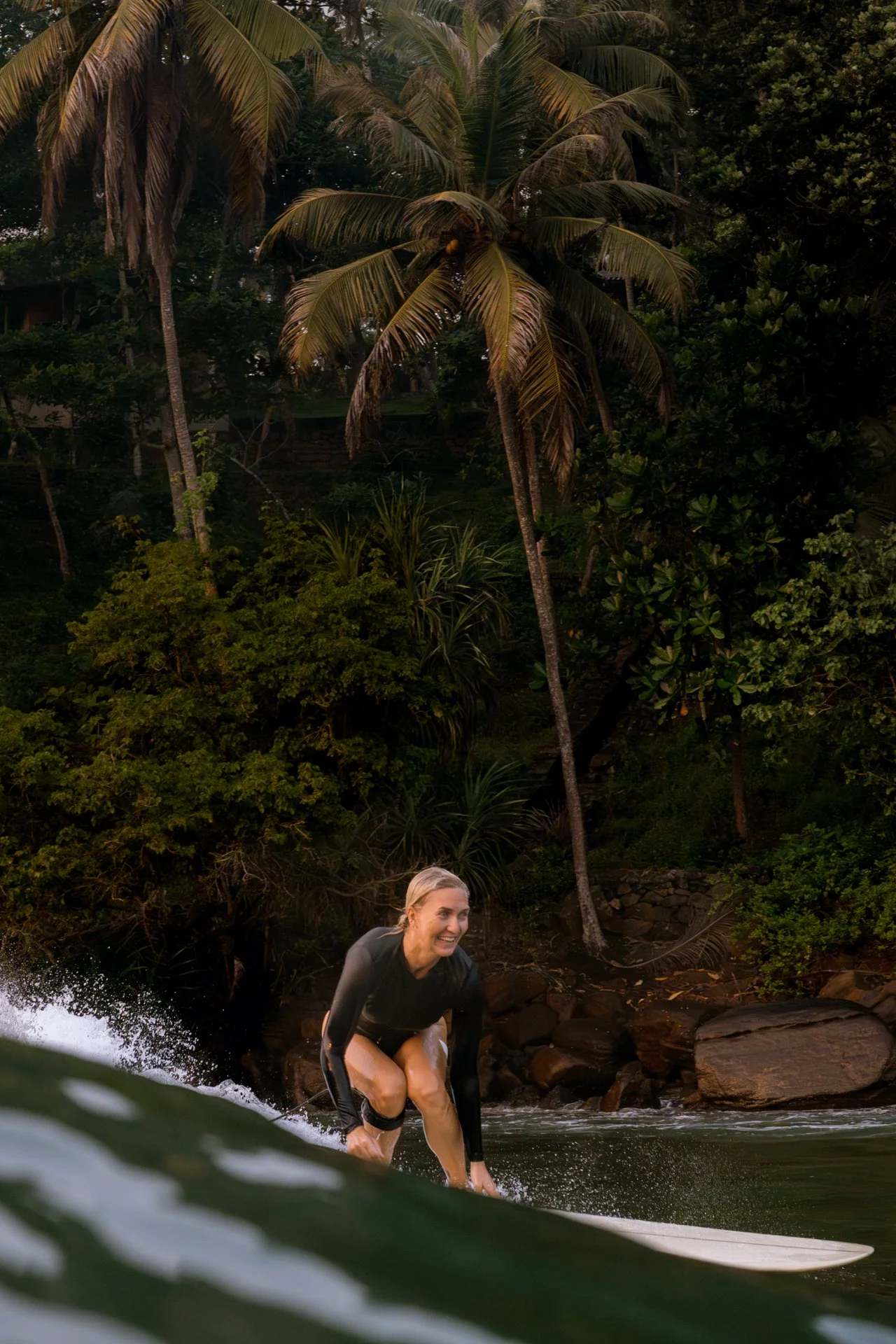 Woman surfing a tropical river mouth surrounded by palms and rainforest.