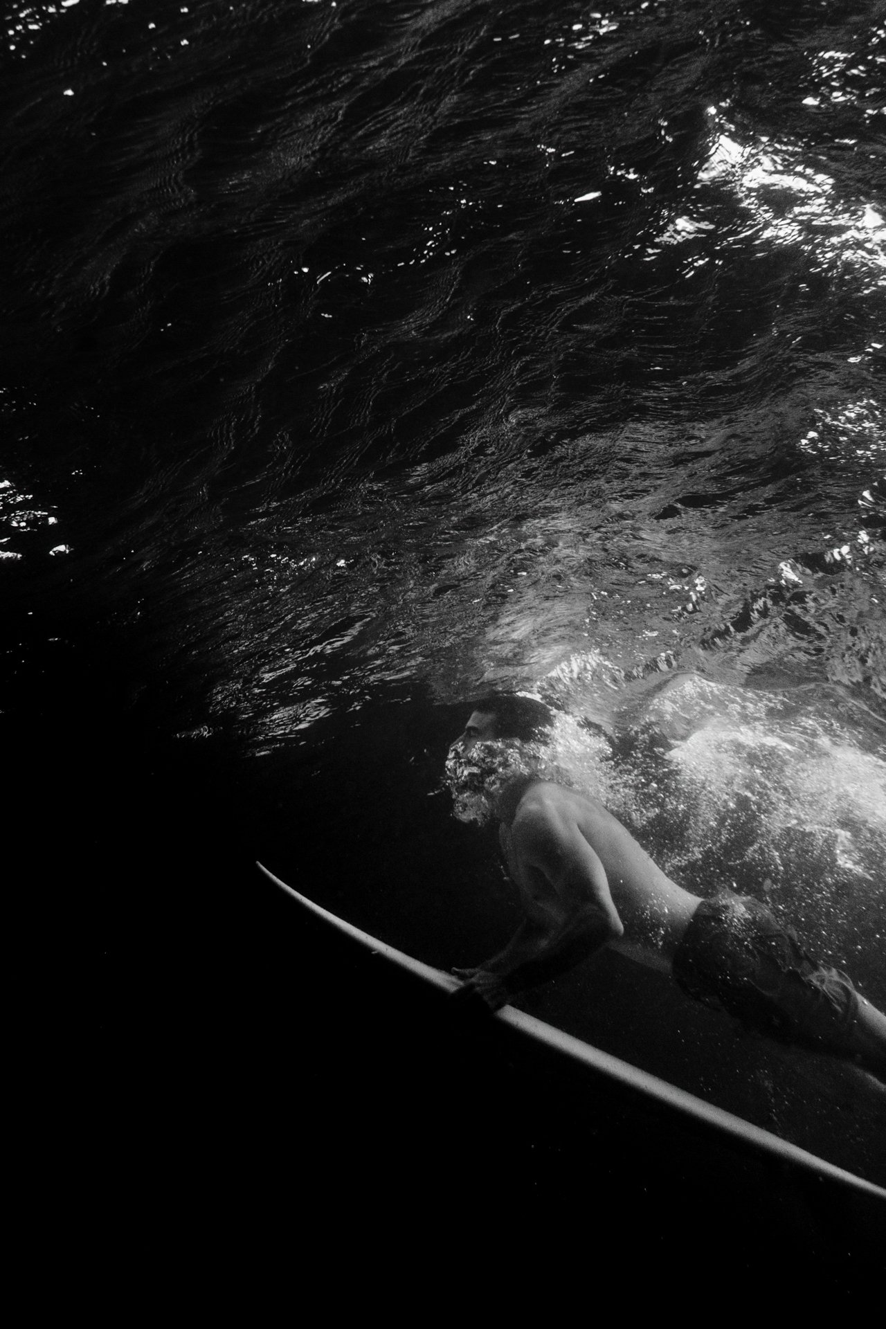 Black and white underwater view of a surfer duck diving beneath the surface. 