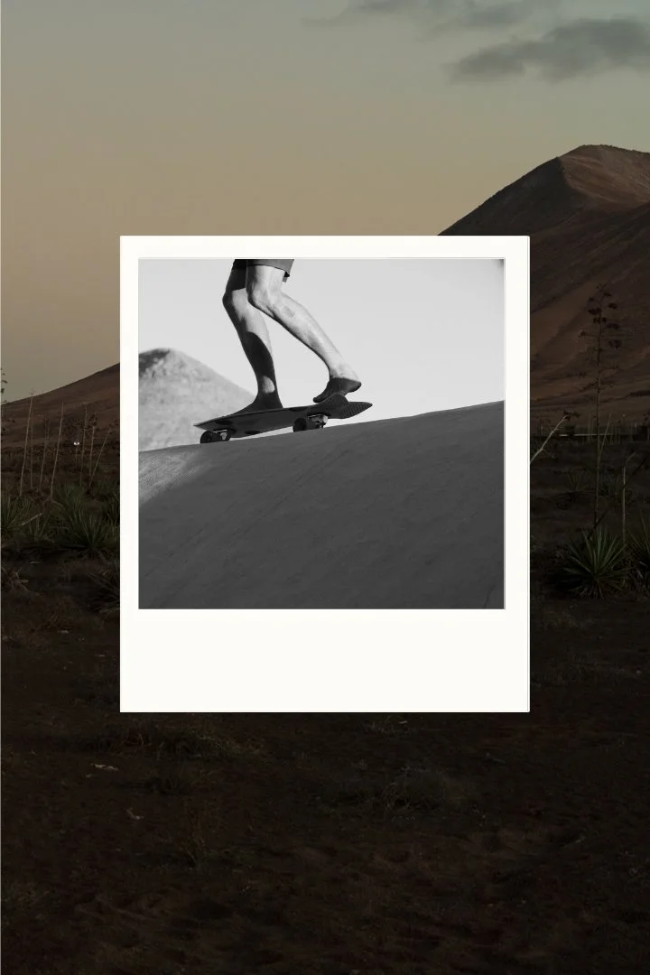 Black and white photograph of a skateboarder riding through a mountain landscape.