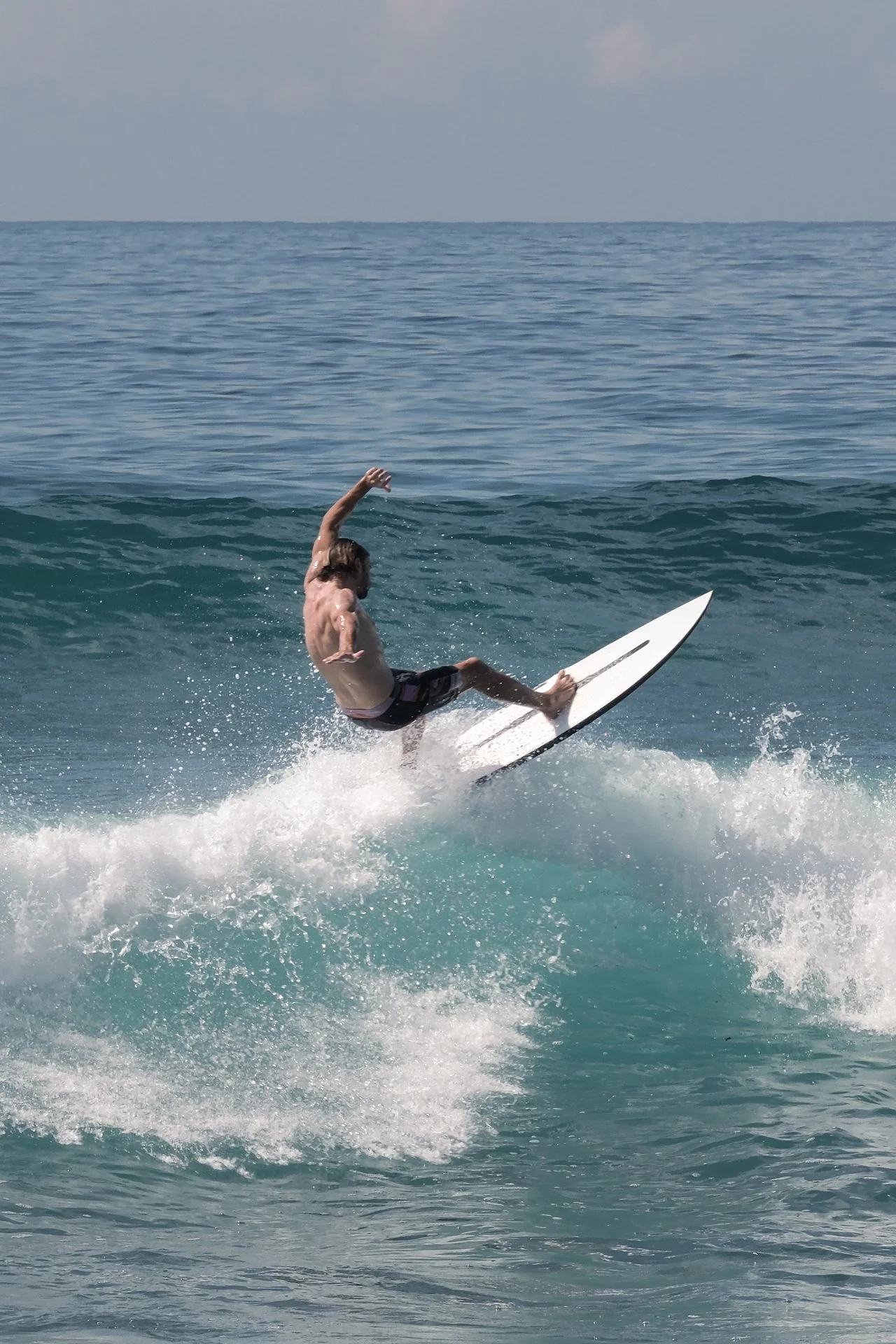 Surfer performing an aerial manoeuvre above a breaking ocean wave.