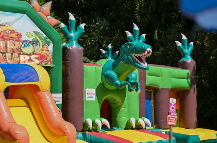 Structure gonflable de parc d'attractions avec un grand dragon vert, des décorations de forêt et des toboggans.