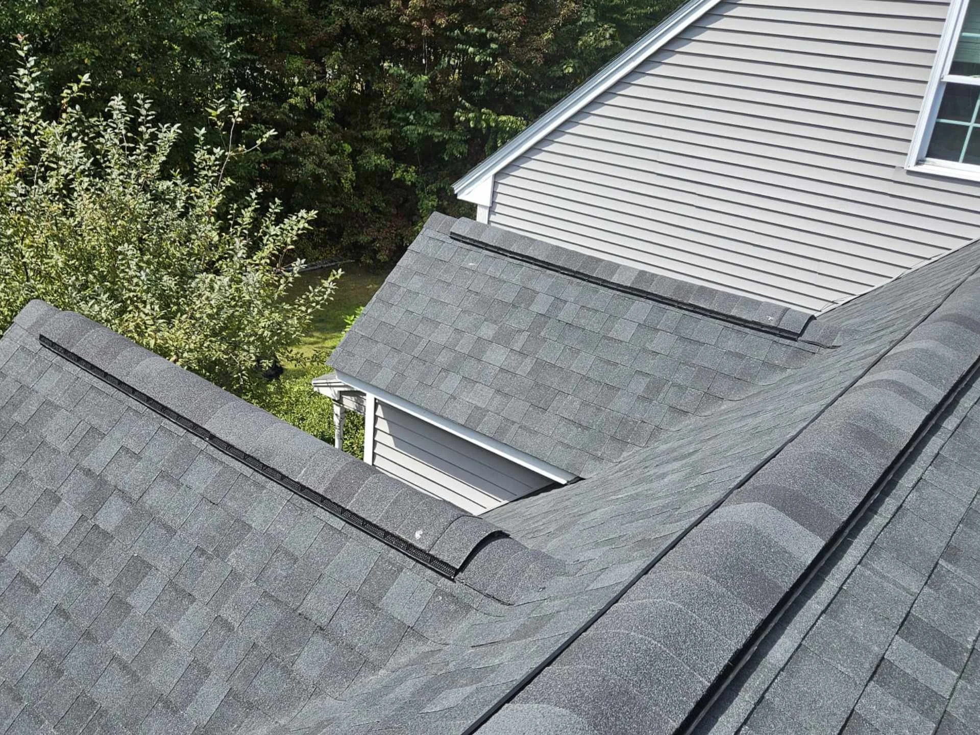 New Asphalt roof in Acton, MA with lush green trees in the background.