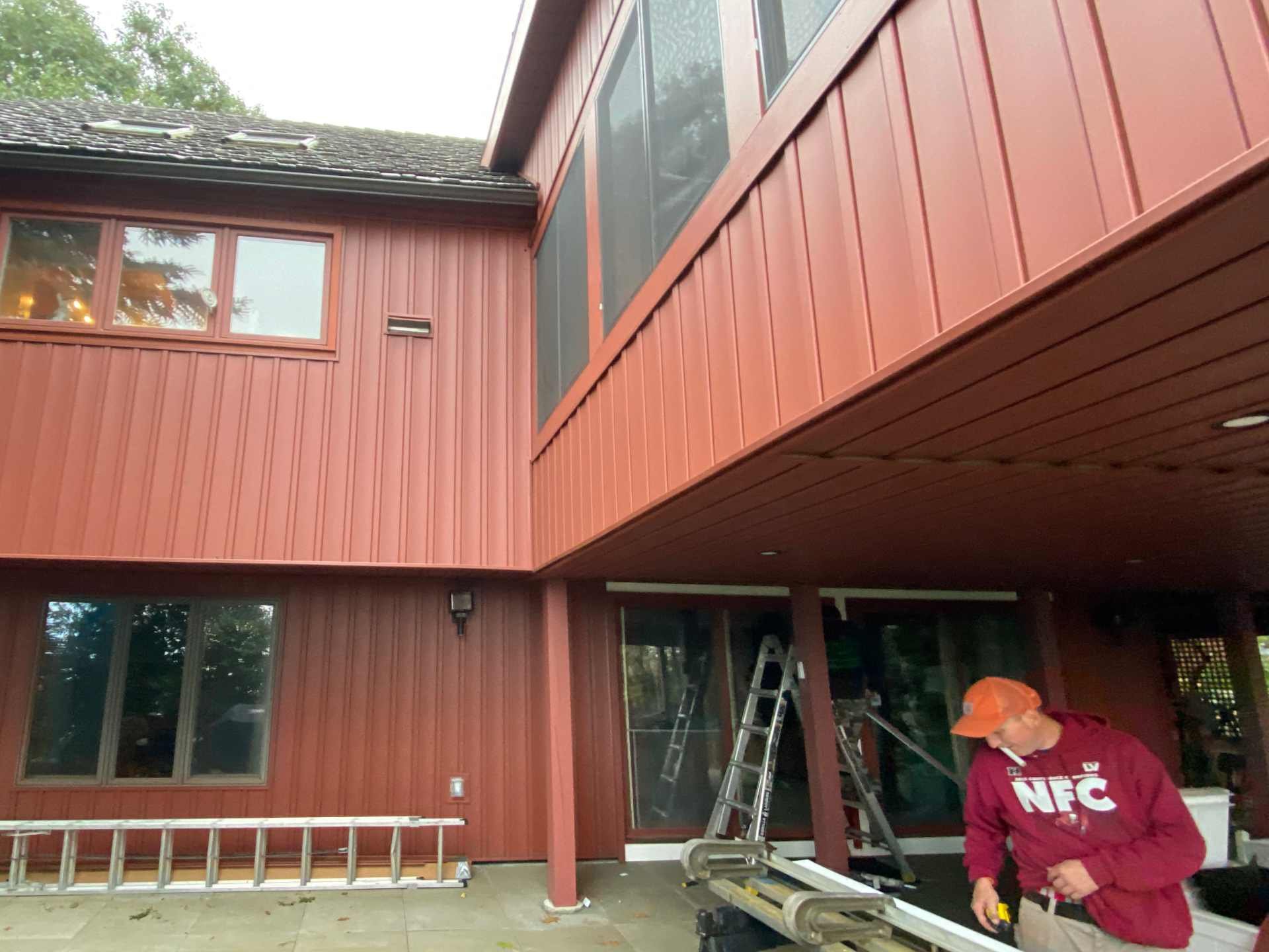 New Certainteed board and batten vinyl siding on a new addition and an existing house with a worker doing detail work with a metal brake. The project also has new windows, PVC trim, and skylights in Princetion, MA completed by McGrath Construction