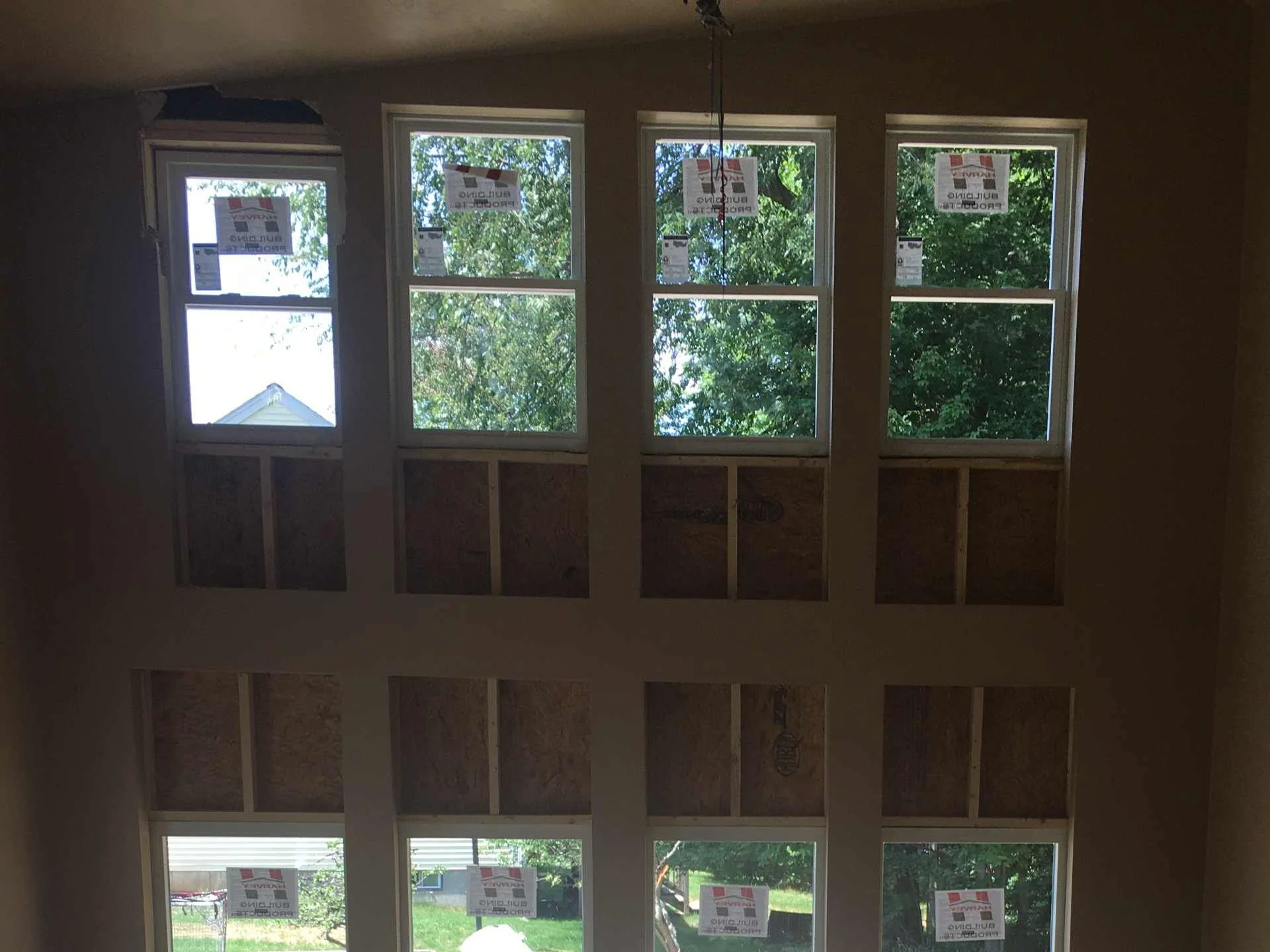 Interior of a house under construction with a wall of six windows, some with signs indicating they are new windows, and trees visible outside in Fitchburg, MA