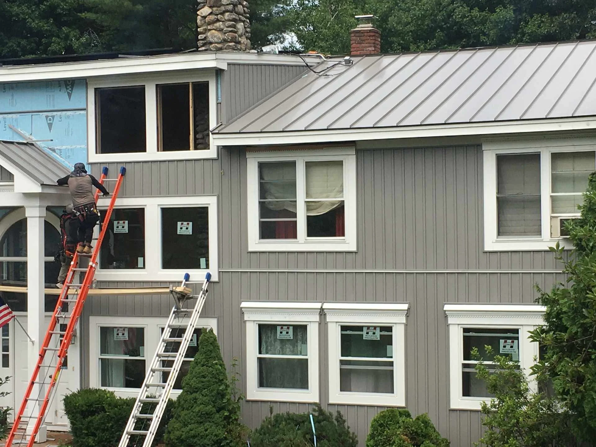 Workers installing standing-seam metal roofing after finishing all the vinyl siding and new energy efficient windows on a house in Fitchburg, MA
