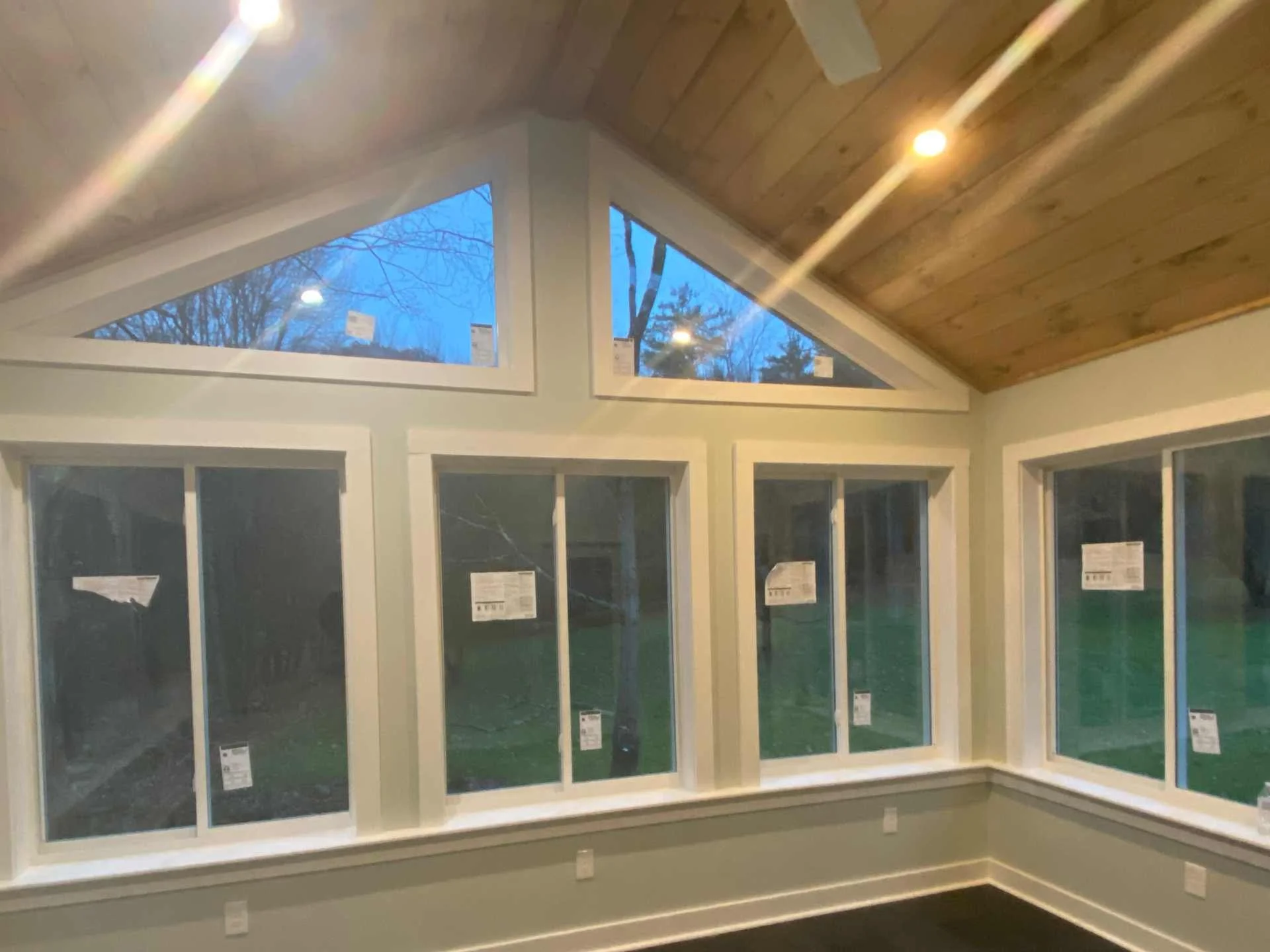 Interior view of a new four season addition with large windows showing trees outside, wooden ceiling, and light fixtures in Winchendon, MA