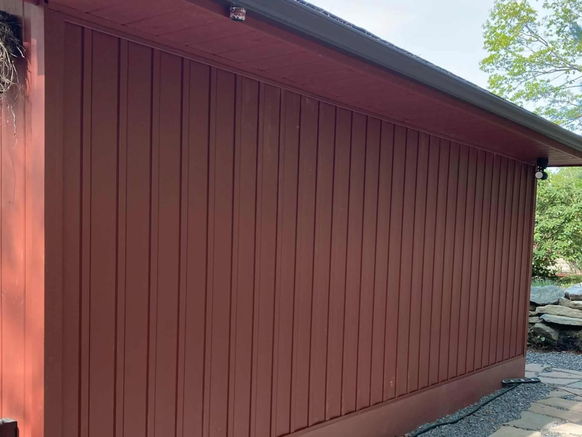 Red vertical vinyl siding on a building exterior with a roof edge and an outdoor security camera in Princeton, MA