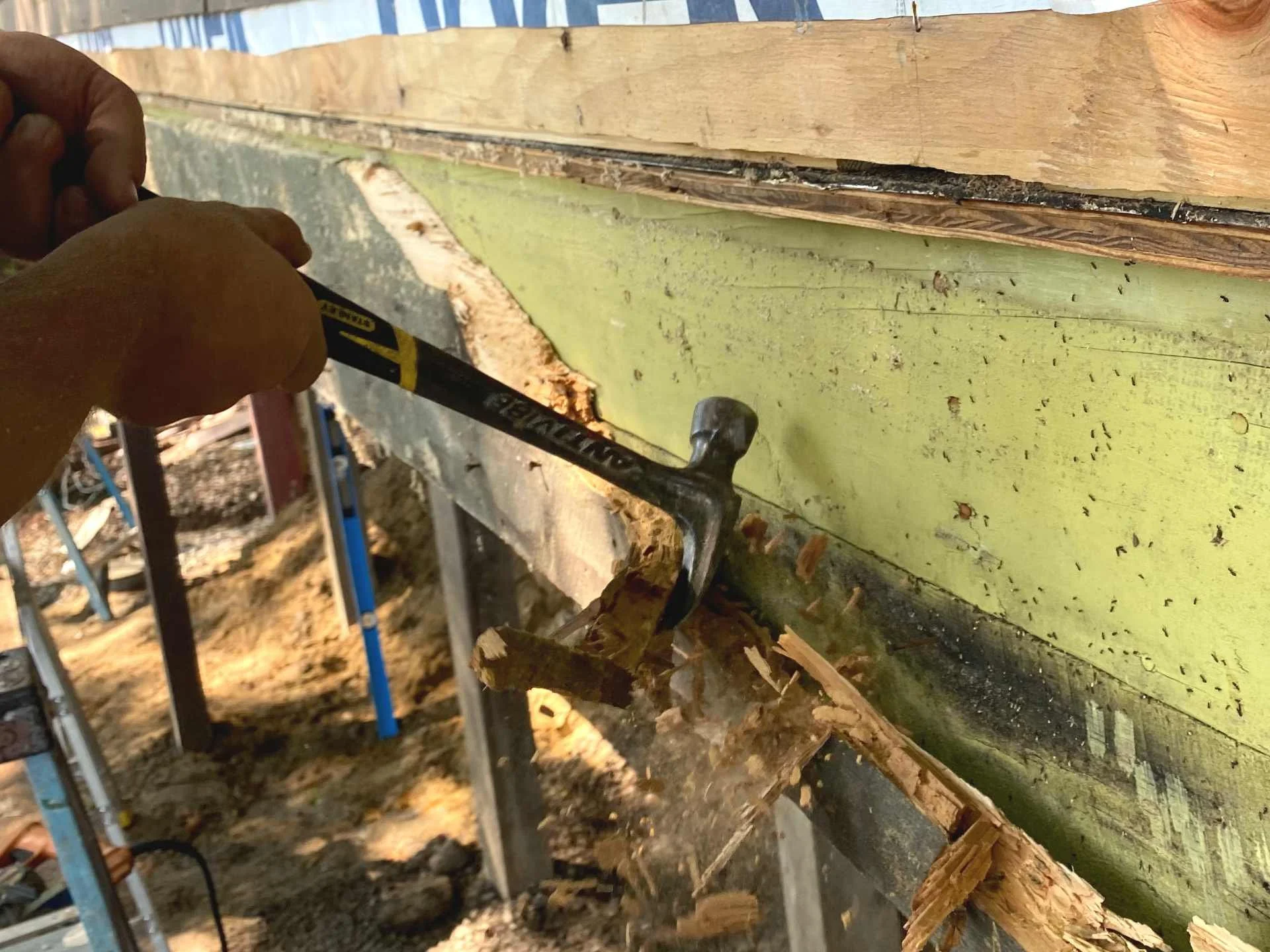 Person using a hammer to remove a damaged wooden beam in a building under renovation in West Boylston, MA