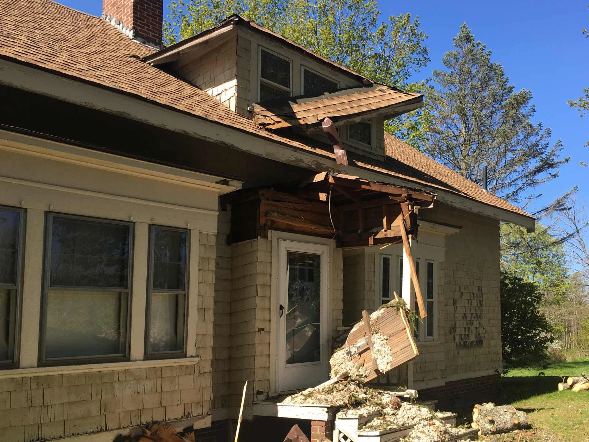 Damaged house exterior by falling tree with partially collapsed roof and debris on the ground in Templeton, MA