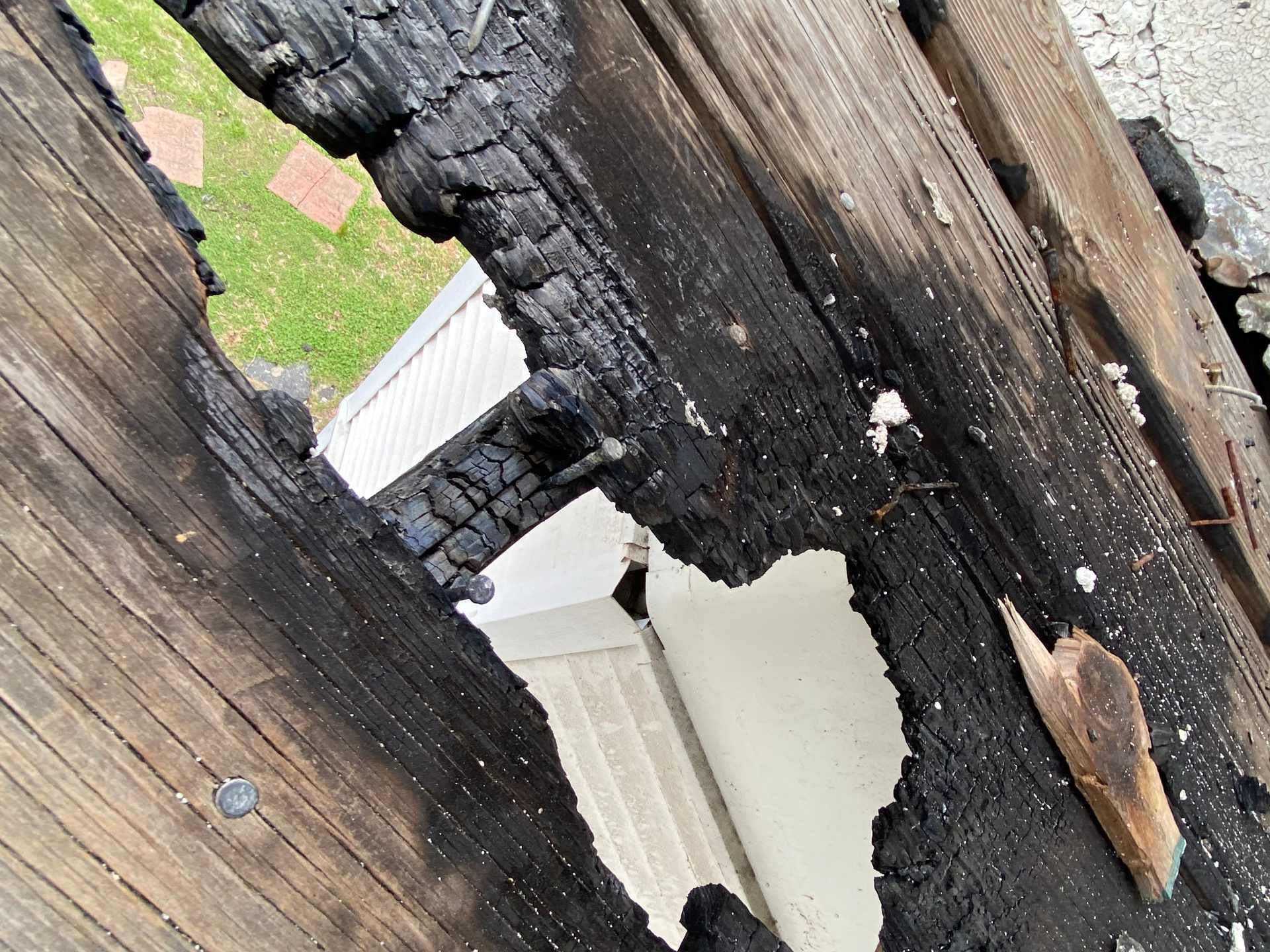 Close-up of a charred, burned wooden beam showing blackened, cracked wood and remnants of nails in Lowell, MA