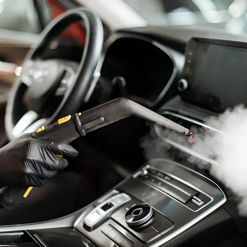 Close-up of a person wearing black gloves cleaning the dashboard of a modern car with a steam cleaner.