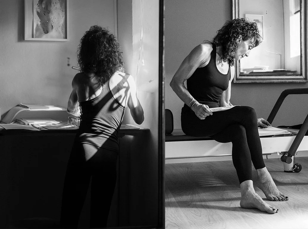 Black-and-white photo of a woman in workout clothes sitting on a Pilates reformer, reflected in a mirror while holding papers.