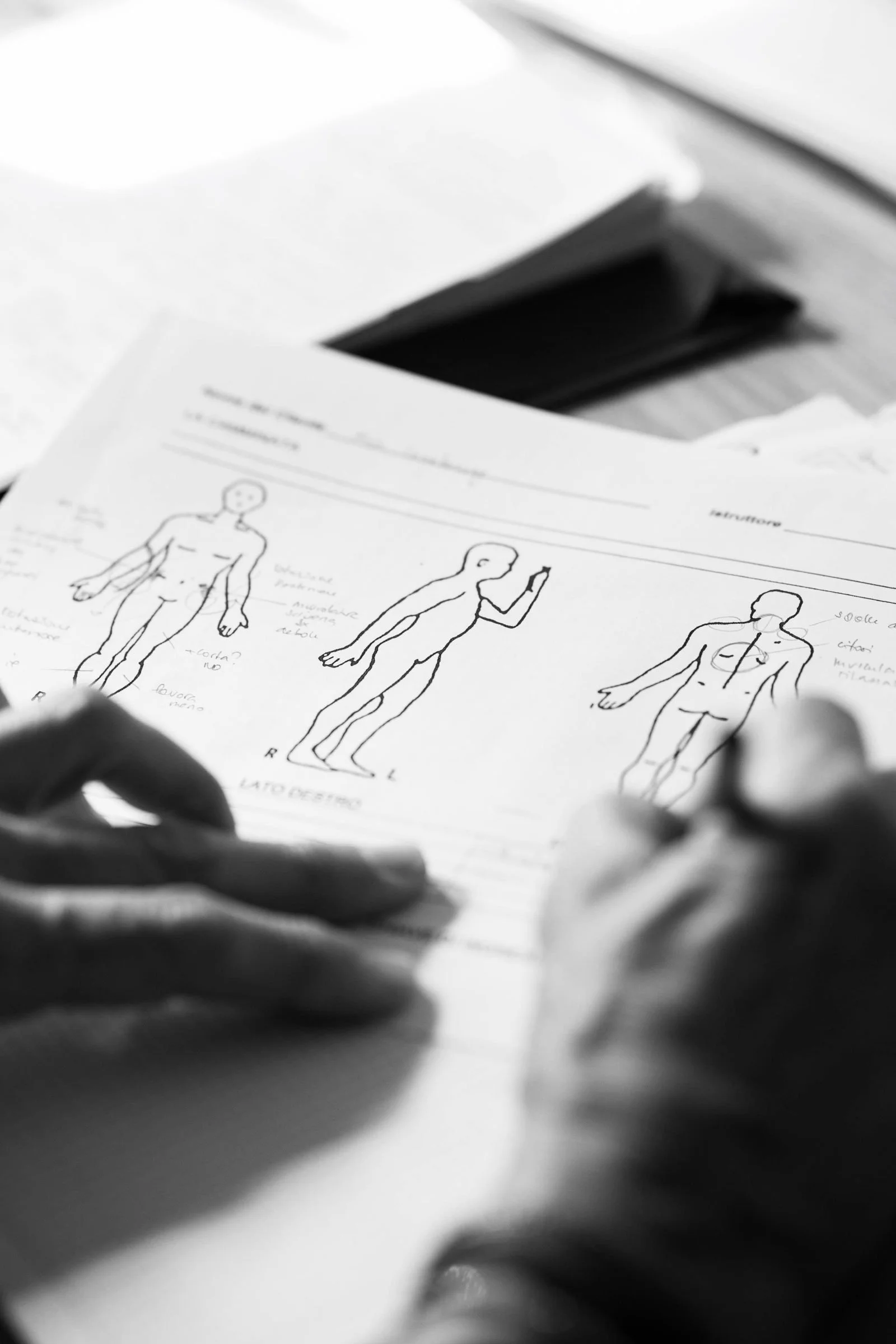 Black-and-white close-up of an artist sketching human anatomical figures on paper with a pencil.