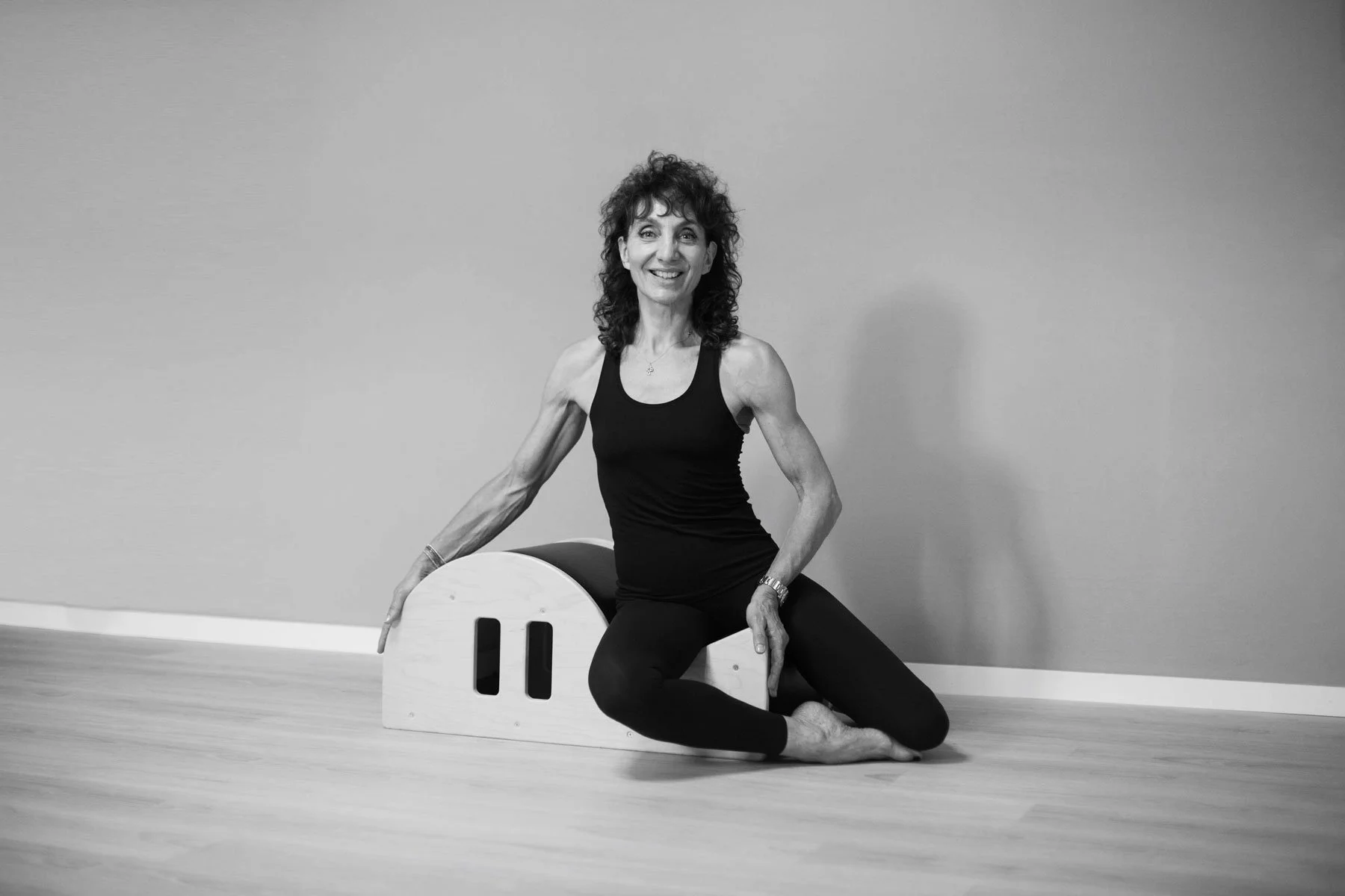 Phaedra Imbert in black workout clothing seated on a Pilates spine corrector in her Studio in Lugano.